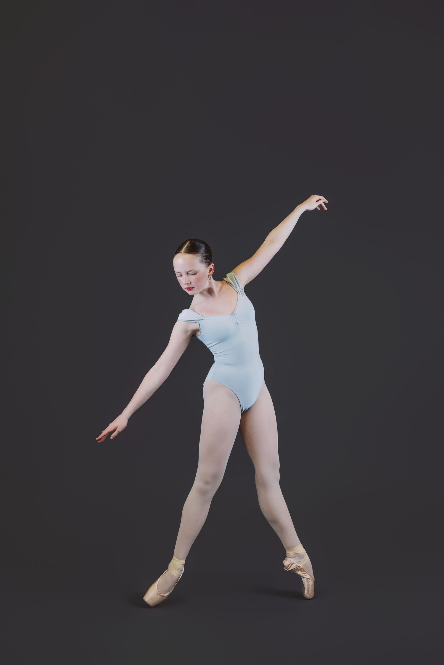 Ballet dancer in light blue leotard performs graceful movements against dark background in four-image sequence.