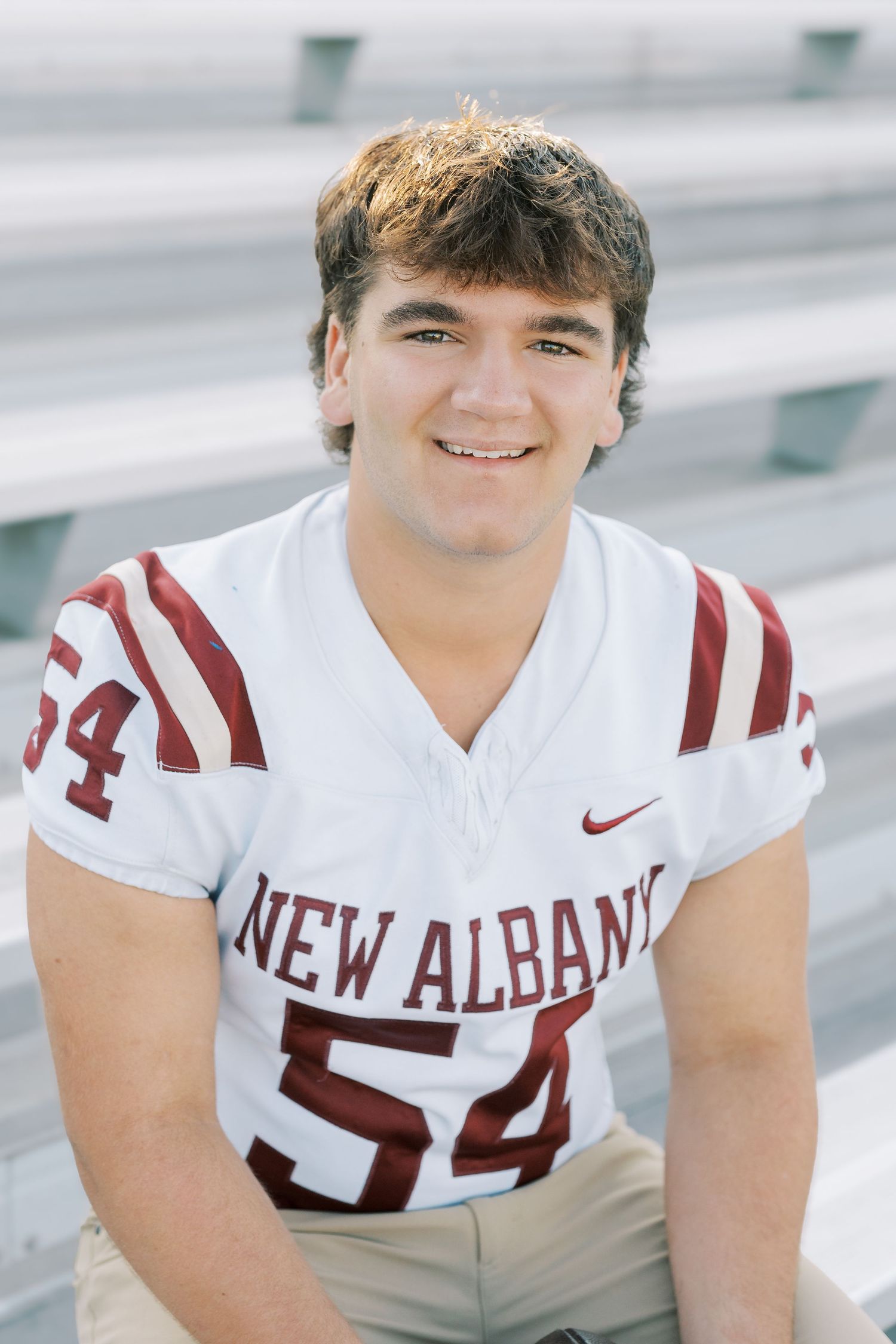 High school football player in white New Albany jersey poses for portrait series on bleachers.