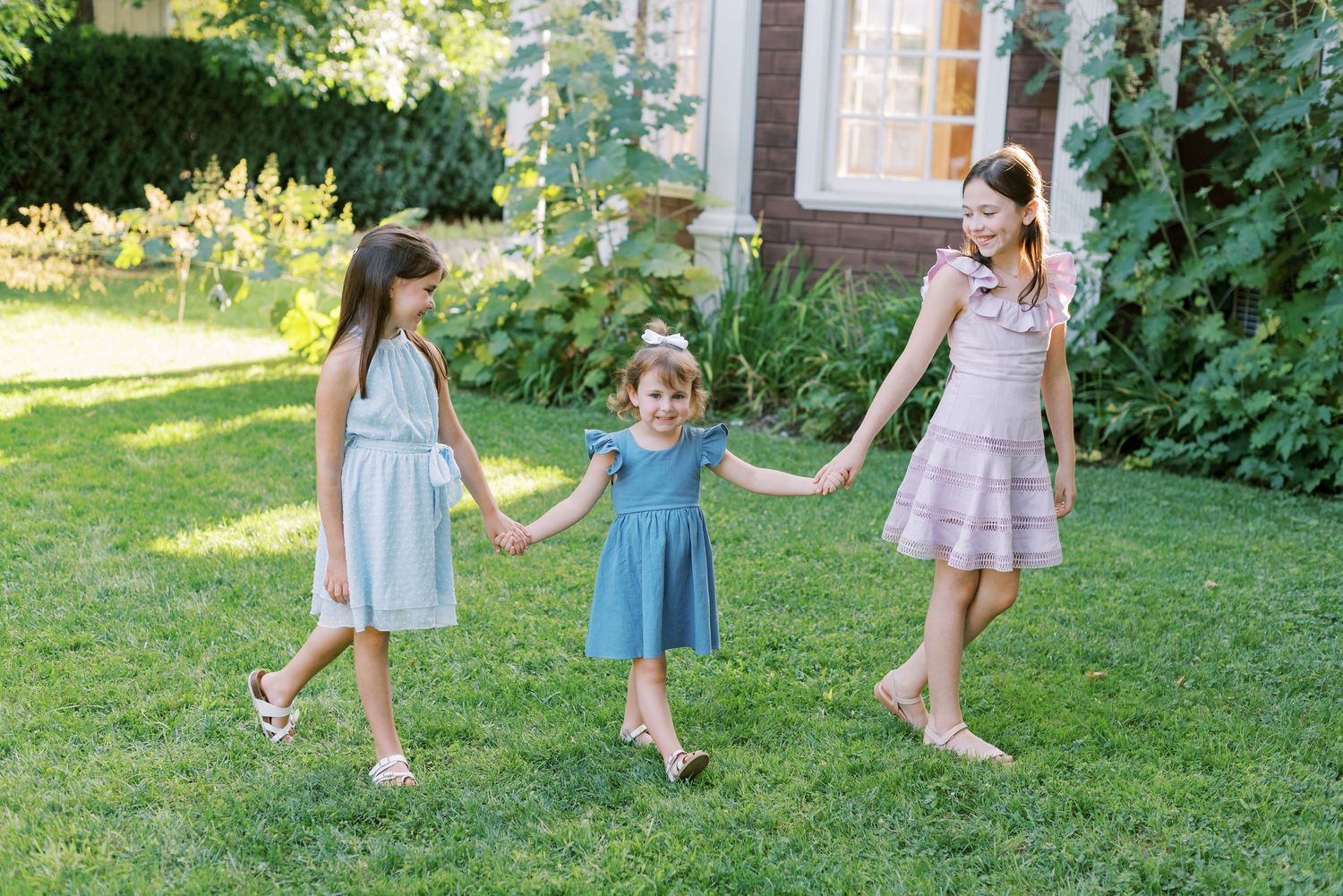 Three young children in summer dresses playing together on a sunny lawn.