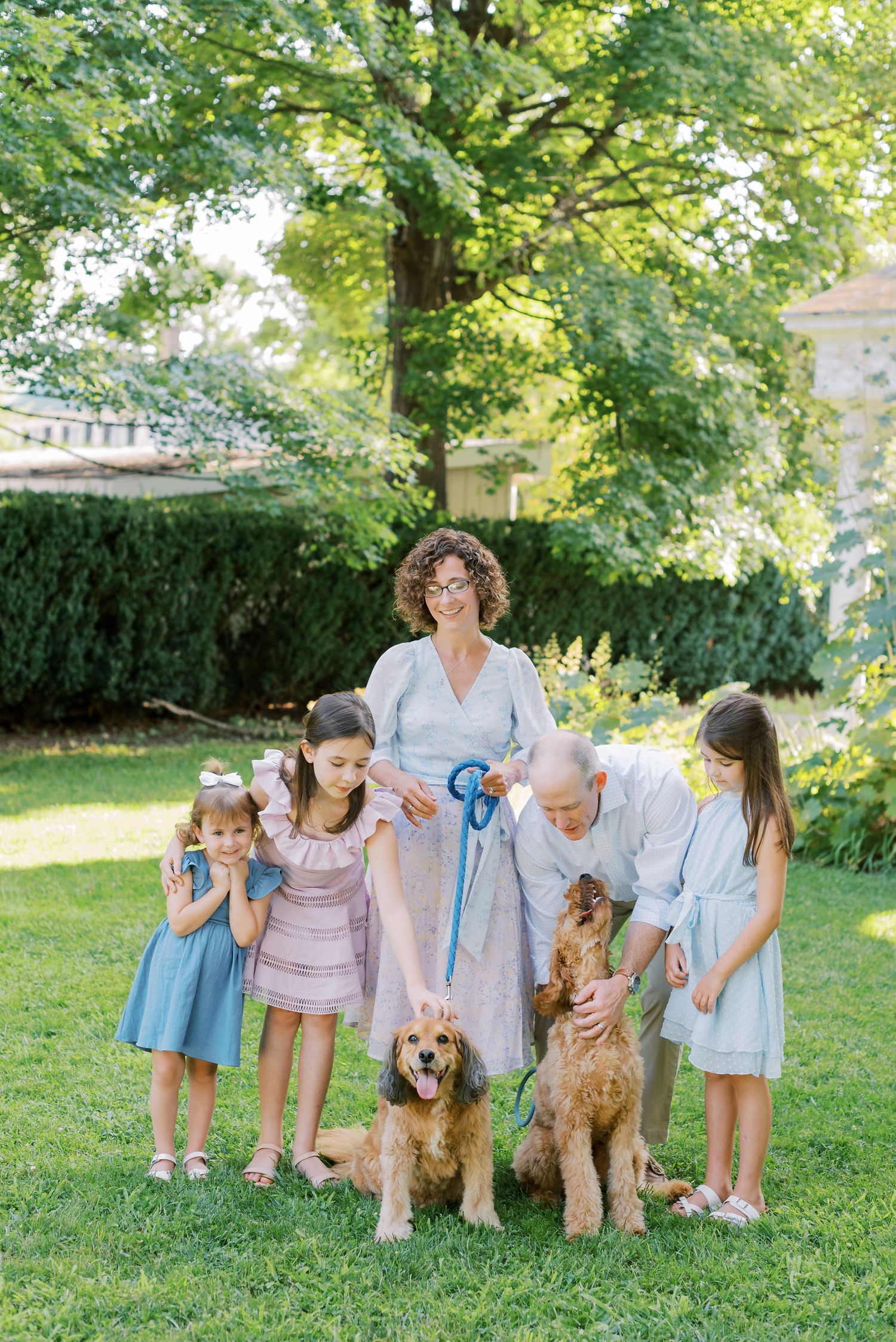 Family members and their golden doodle dogs gather for outdoor photos on a green lawn in summer.
