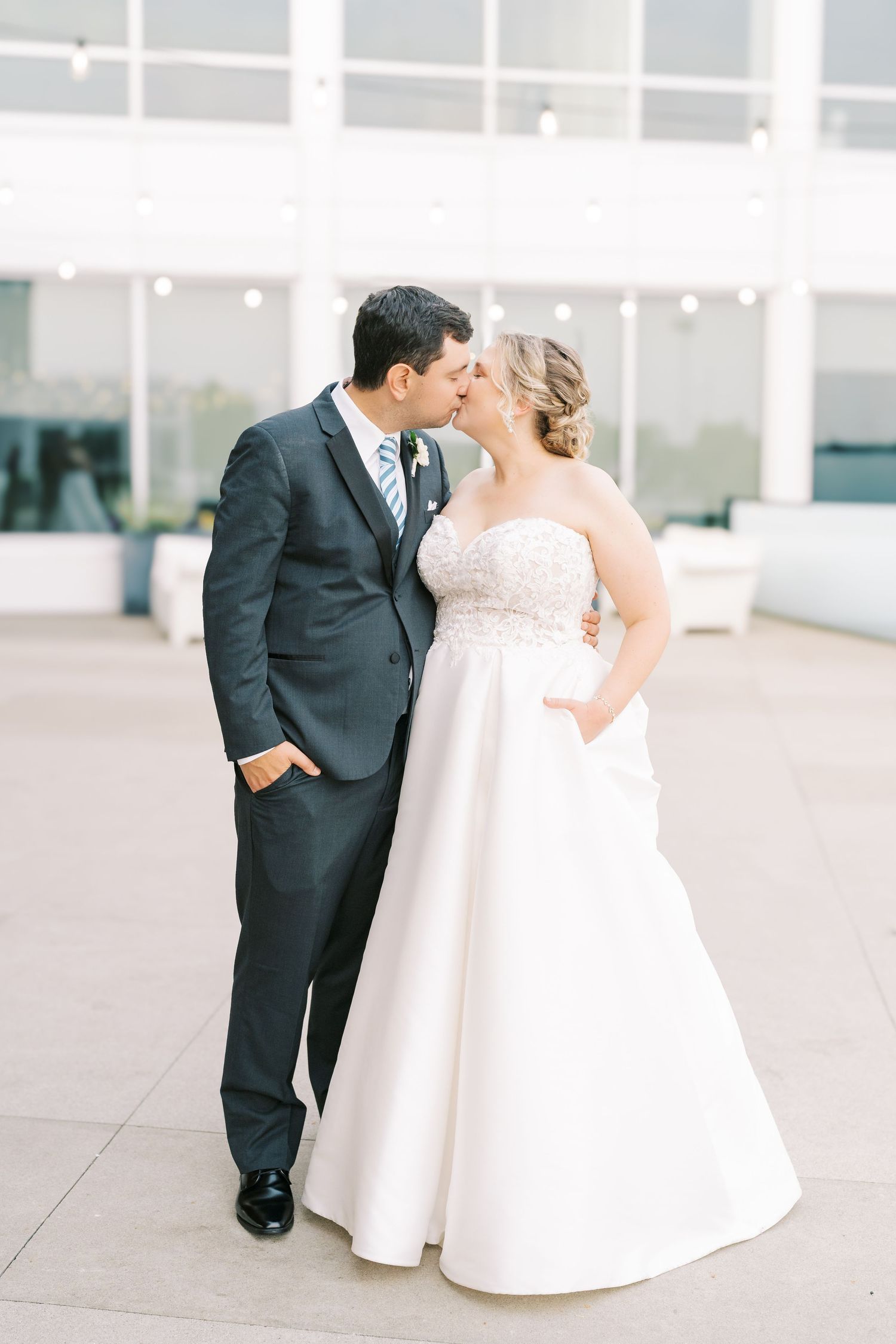 A romantic wedding couple shares an intimate moment in formal attire against a light modern backdrop.