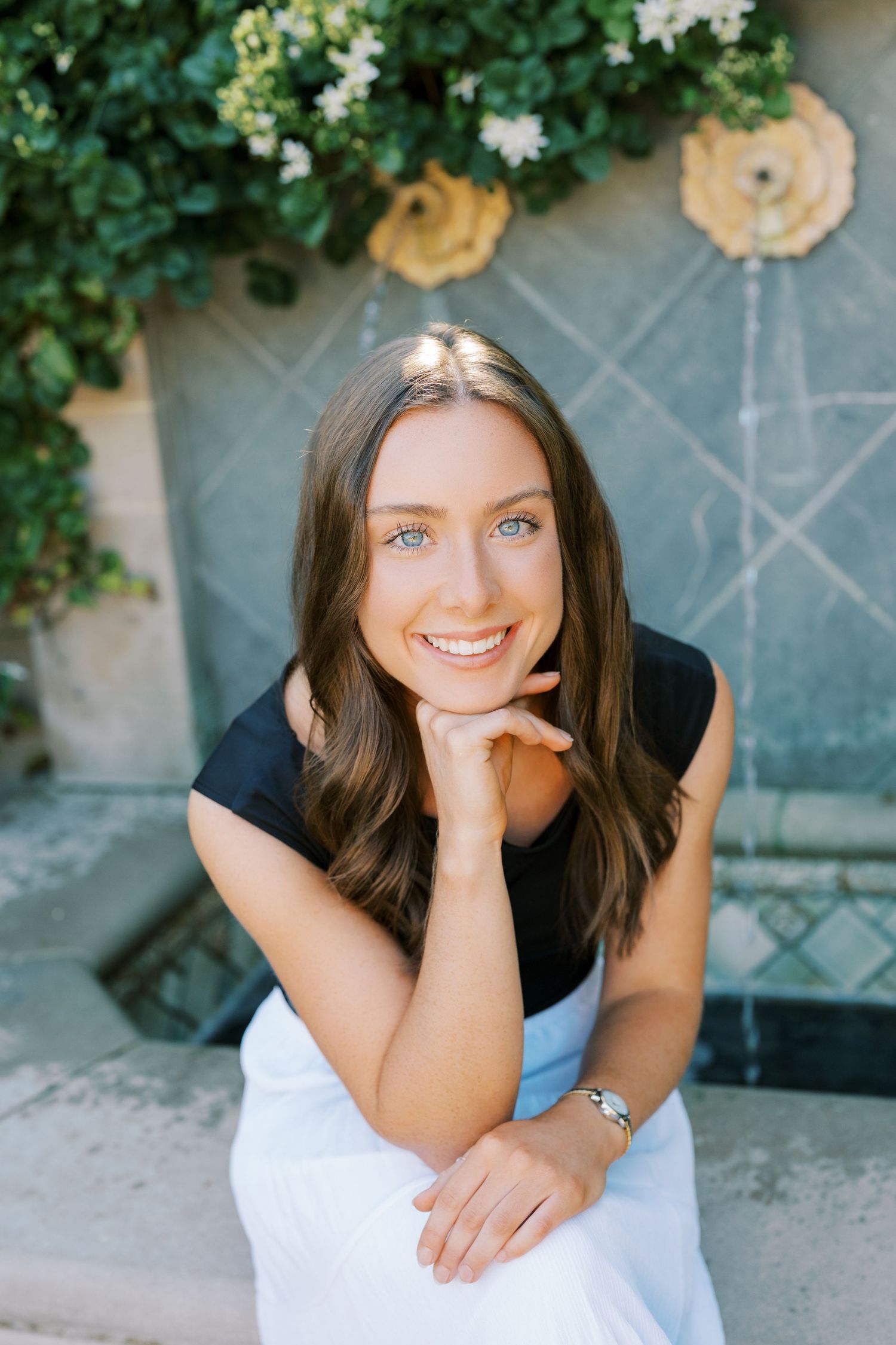 A series of candid outdoor portrait shots showing someone in a black top and white skirt against a stone wall with greenery.