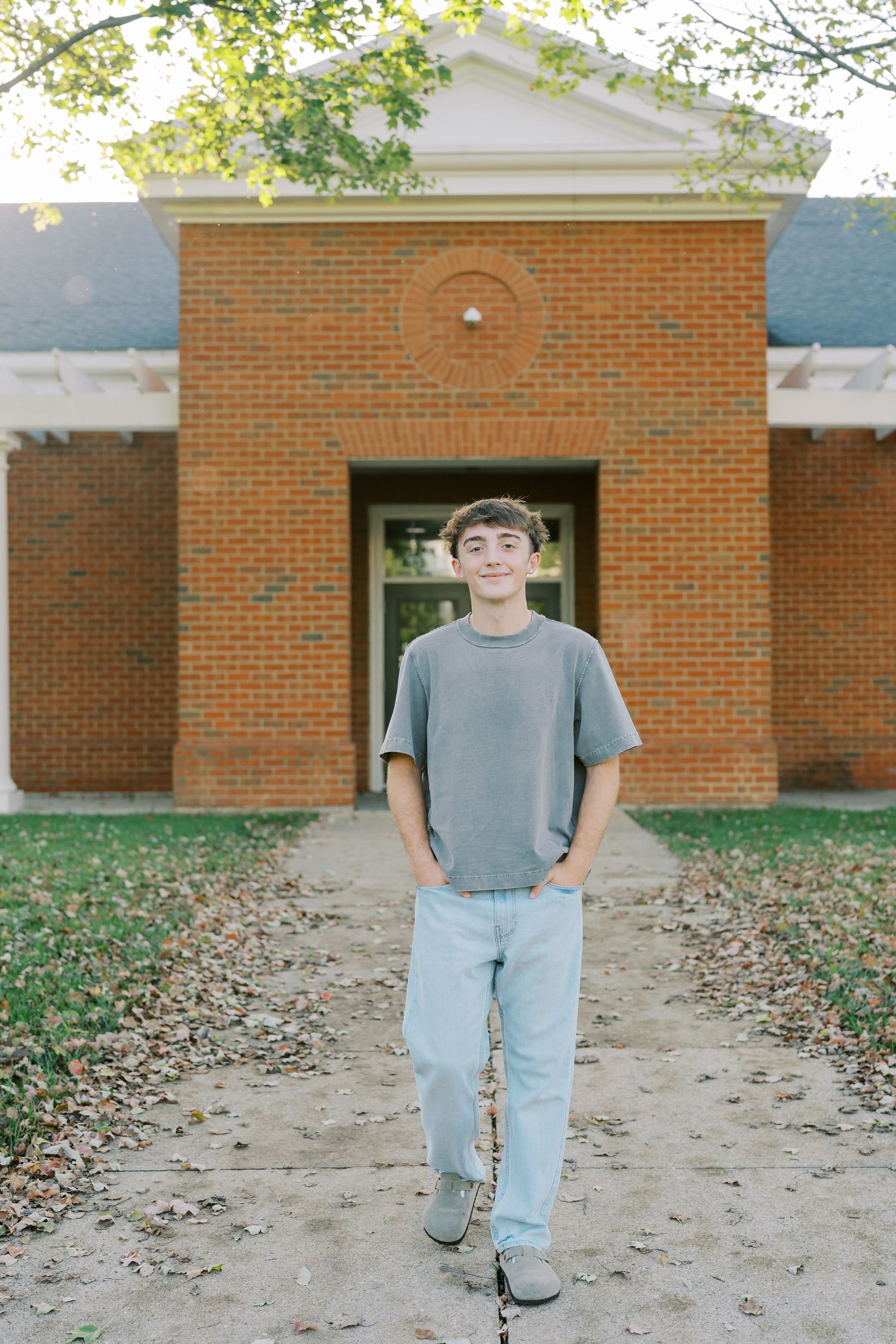 A sequence of five photos showing someone in a gray shirt and jeans walking across a leaf-covered path near a brick building.