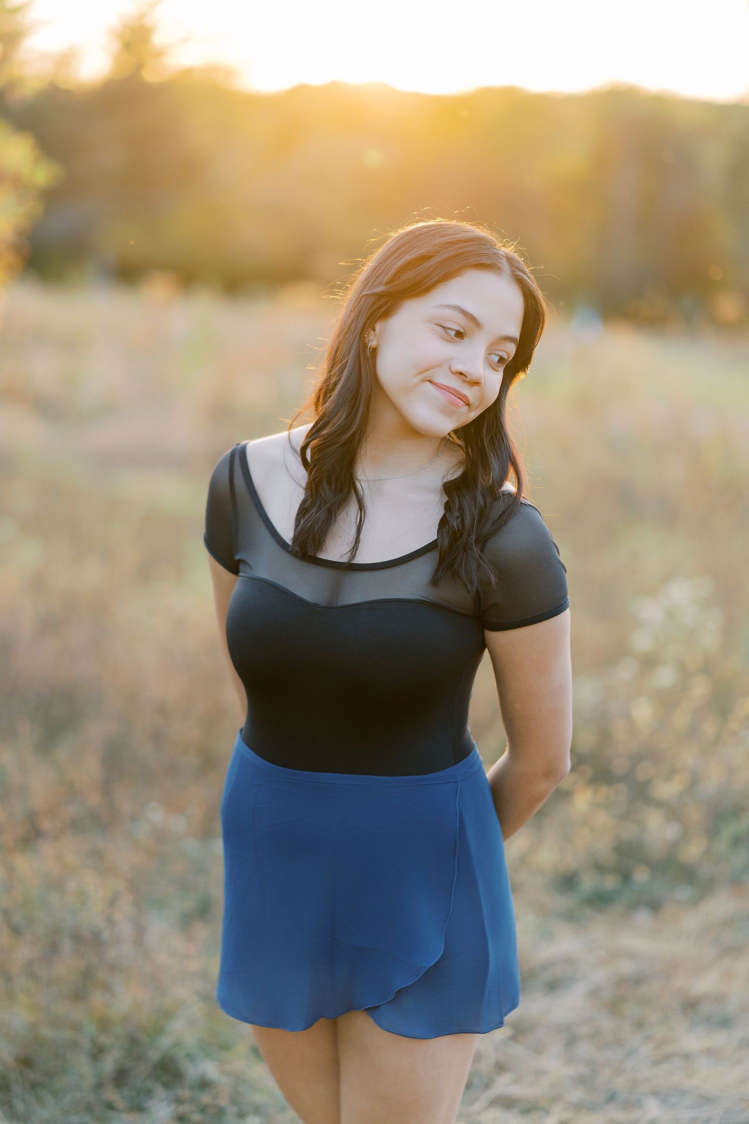 A person in a black and blue dress poses in a golden field at sunset.