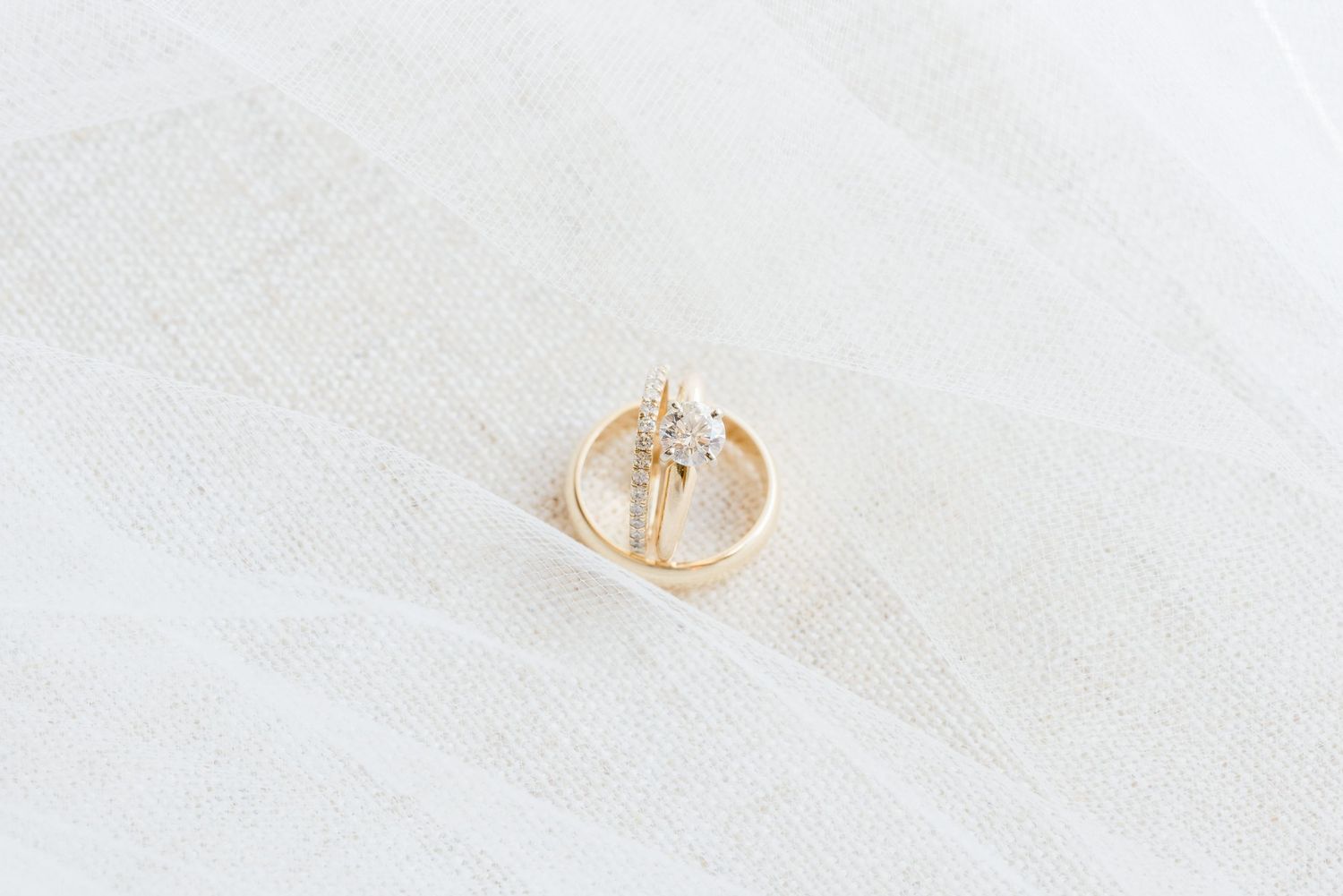 A pair of delicate gold hoop earrings with small pearls displayed on a white textured surface.