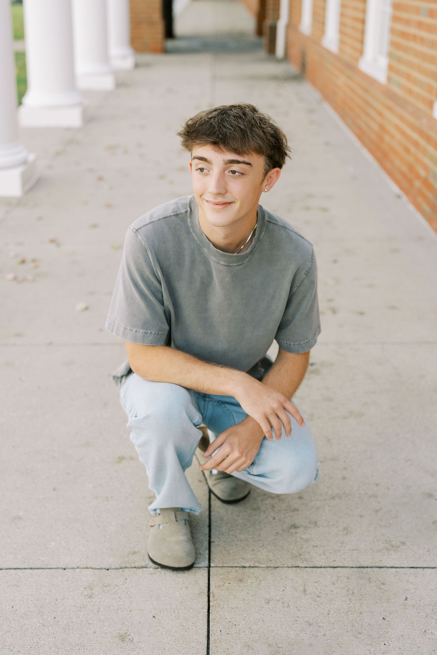 A person in a gray sweater and light jeans sits casually on concrete steps against a brick wall.