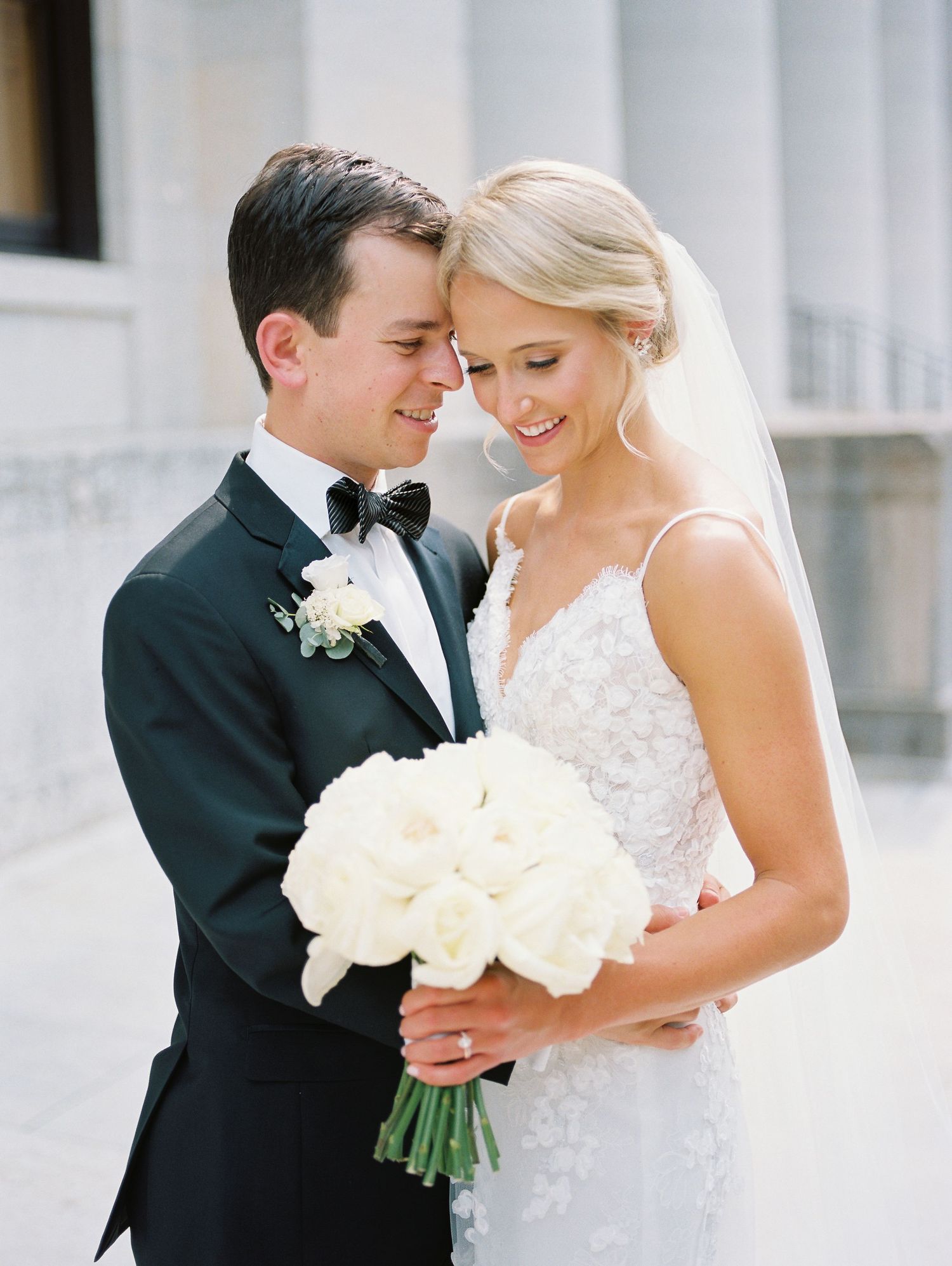 Romantic wedding couple embracing outdoors near white columns.