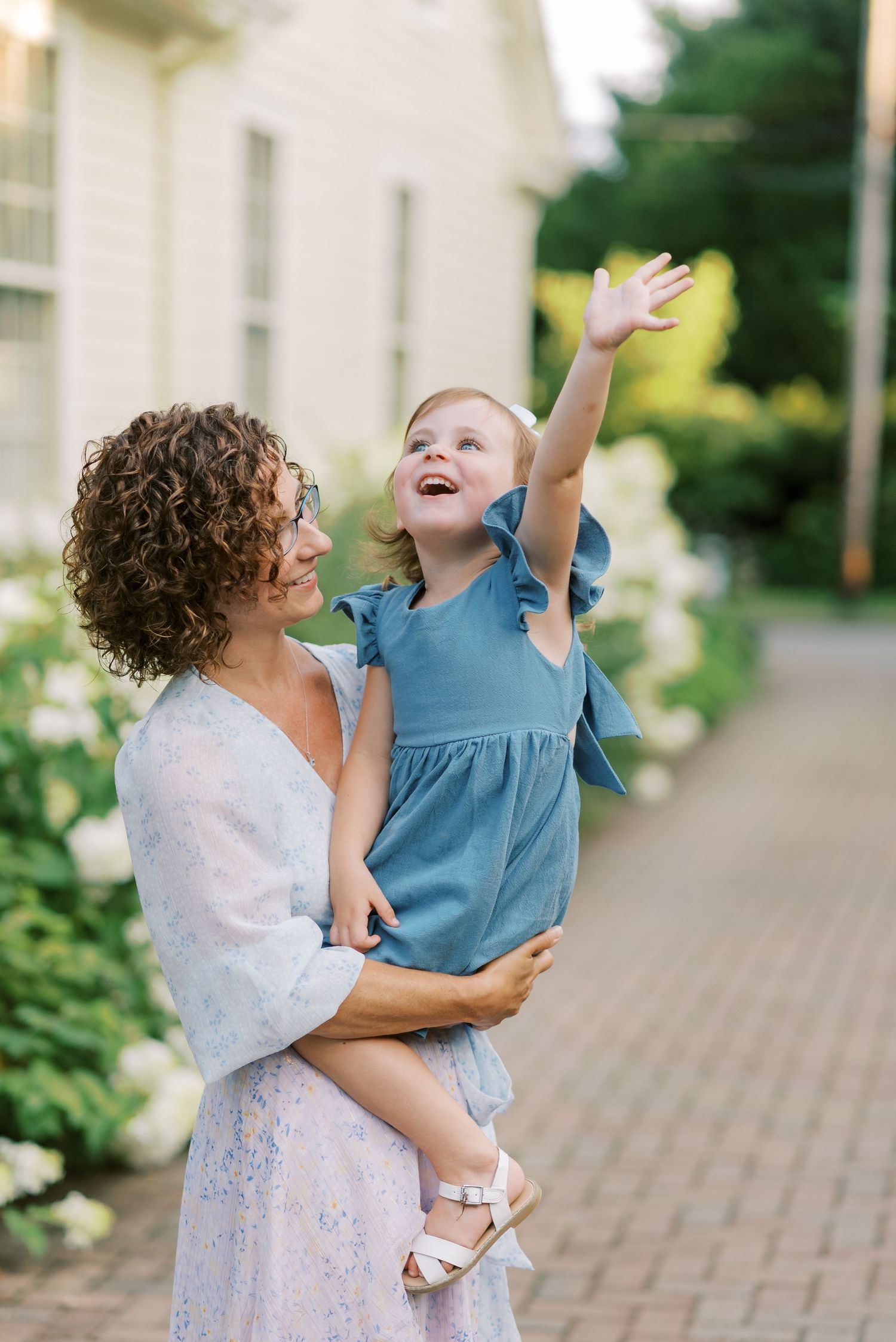 Parent and child sharing joyful moment outdoors on brick path with hydrangea garden.