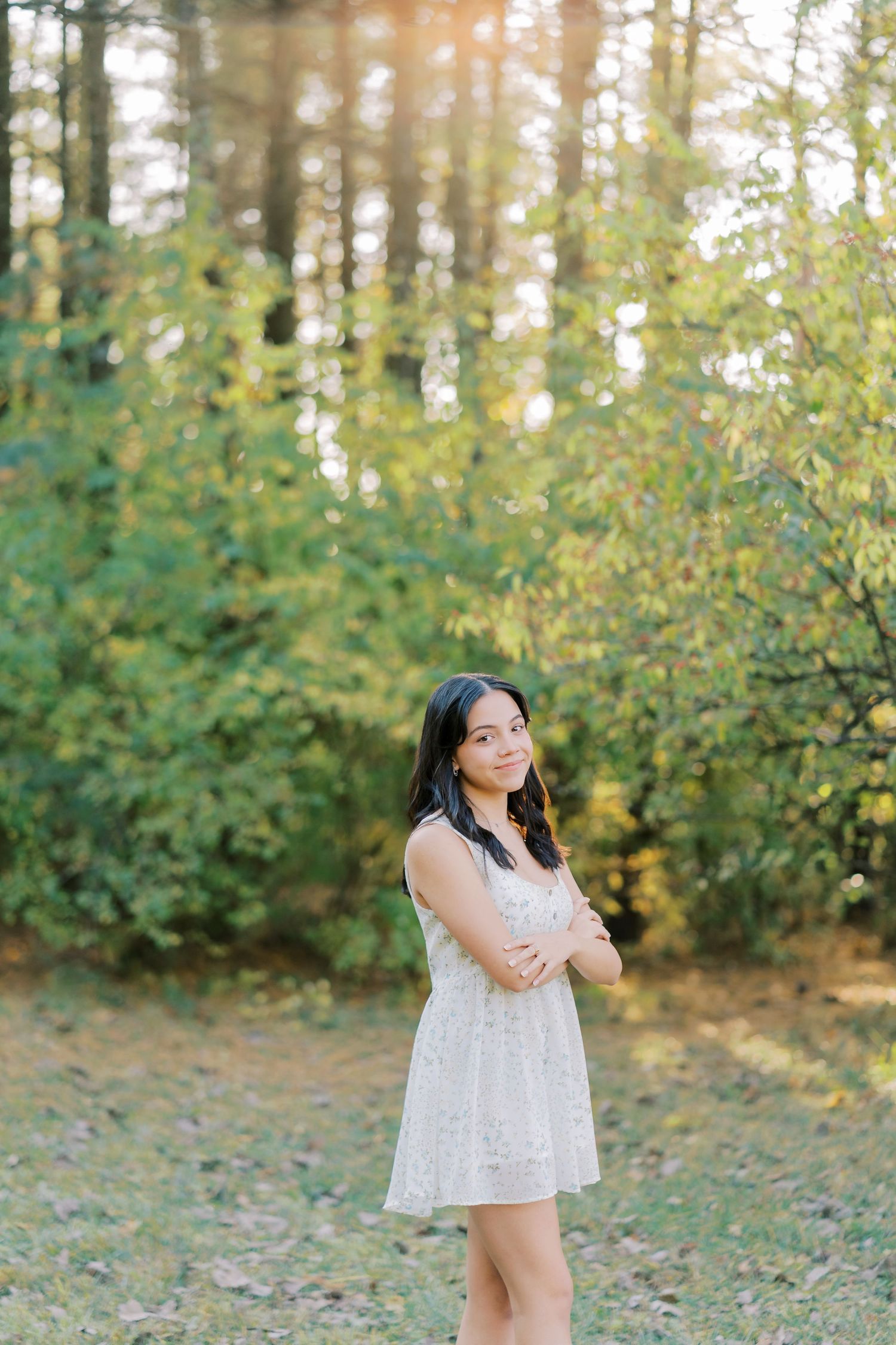 A person in a white lace dress poses in a sunlit forest clearing surrounded by green trees and foliage.