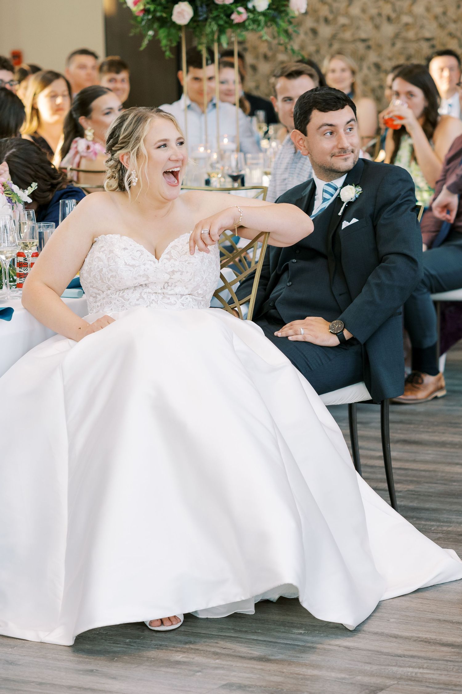 Wedding reception guests seated at tables with white tablecloths in an elegant indoor venue with romantic lighting.