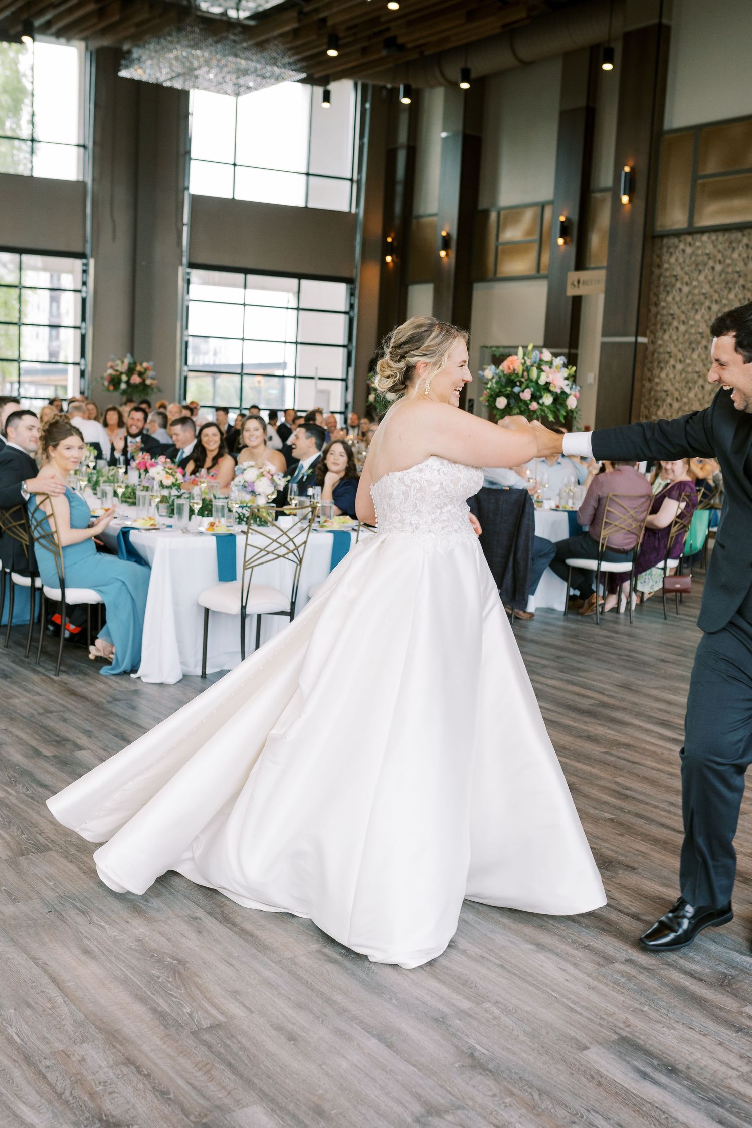 Wedding reception guests watch as couple shares their first dance on a rustic wood floor in an elegant venue.