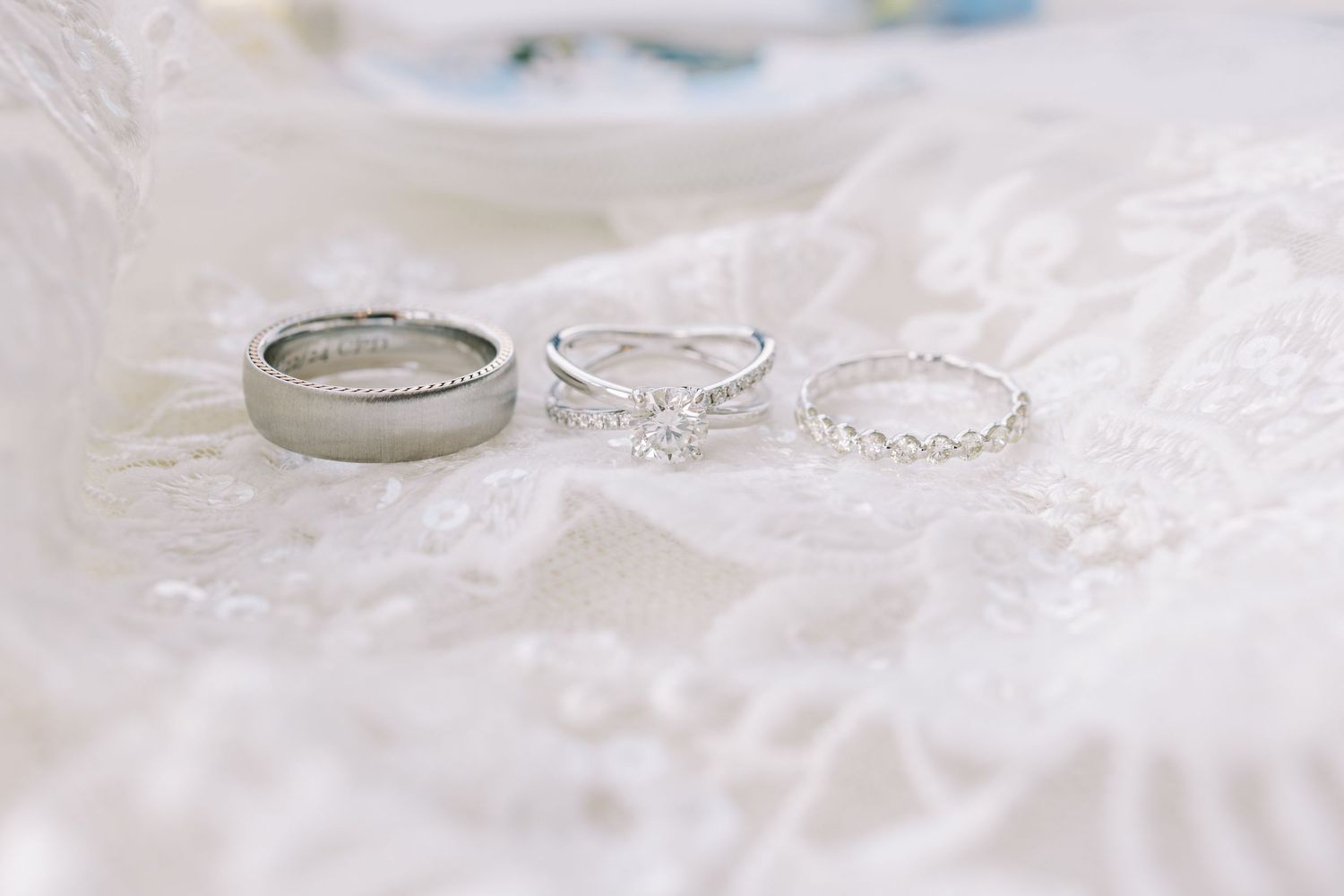Delicate lace wedding dress details and silver jewelry accessories arranged on white fabric.