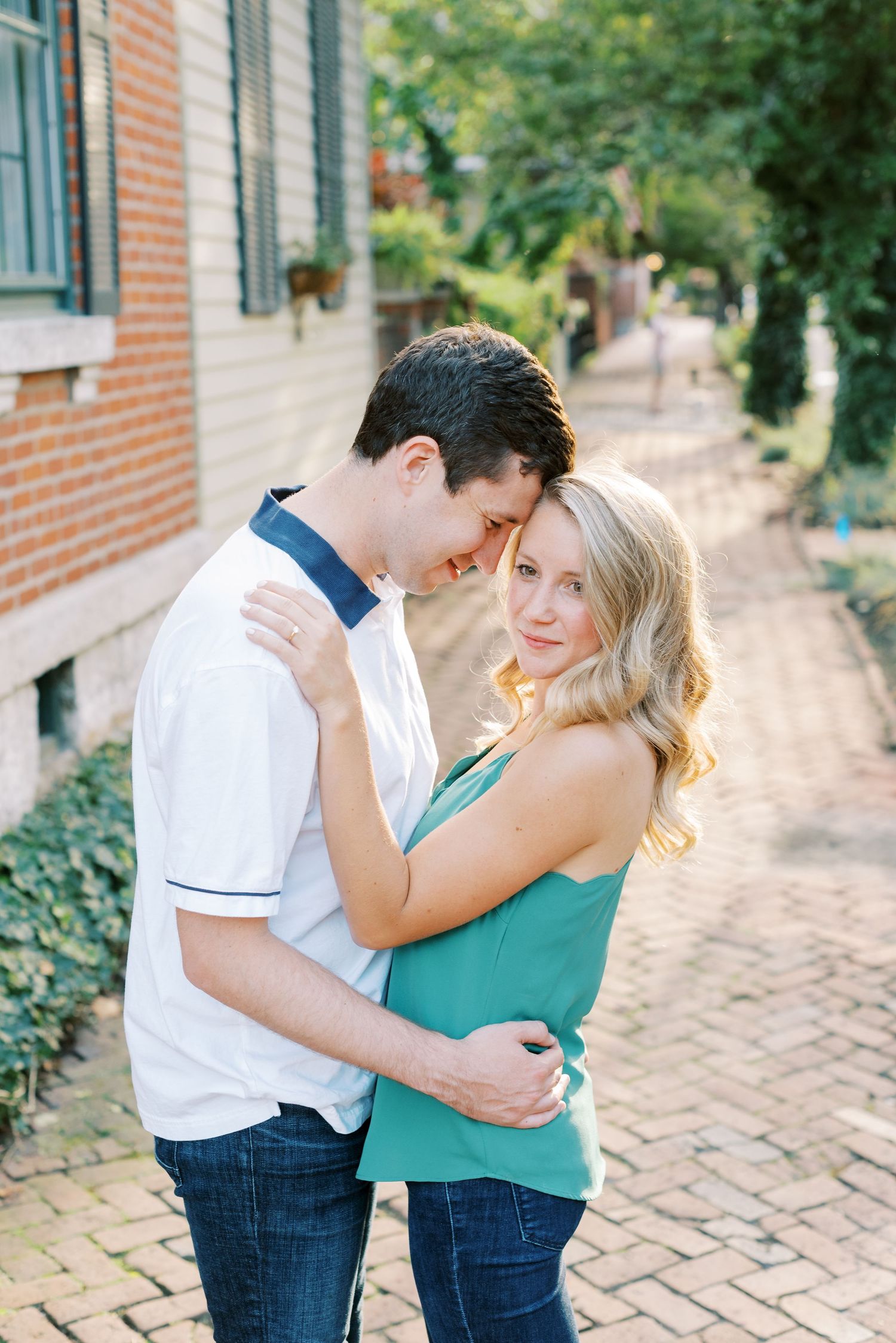 A couple in casual attire shares intimate moments on a brick pathway near a building.