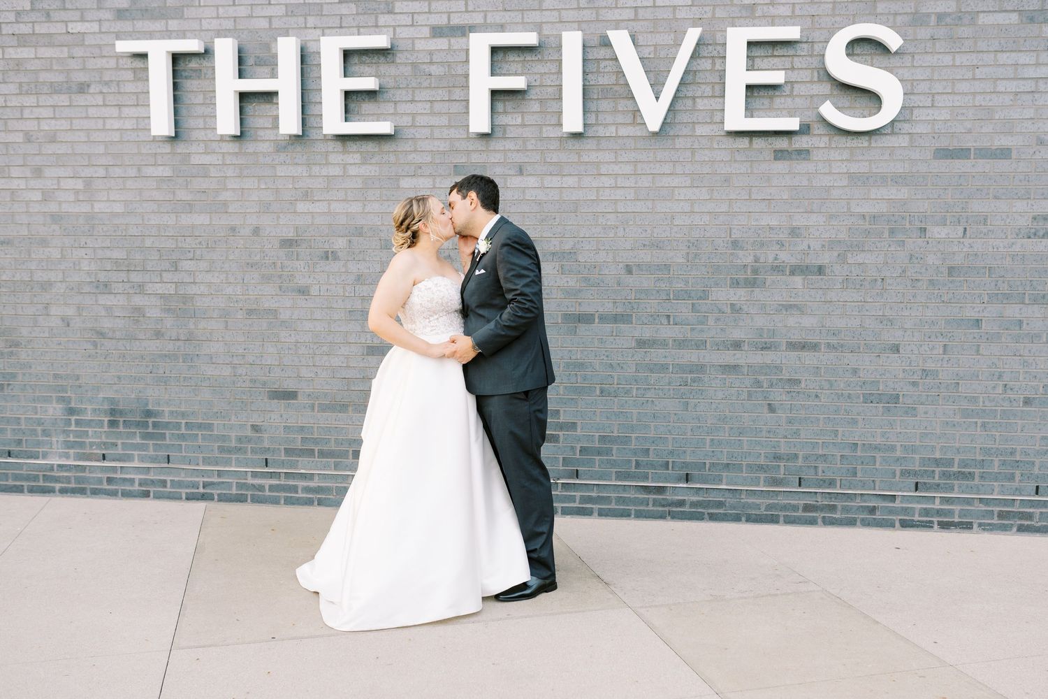 A series of five wedding photos showing a couple in formal attire posing against a gray brick wall.