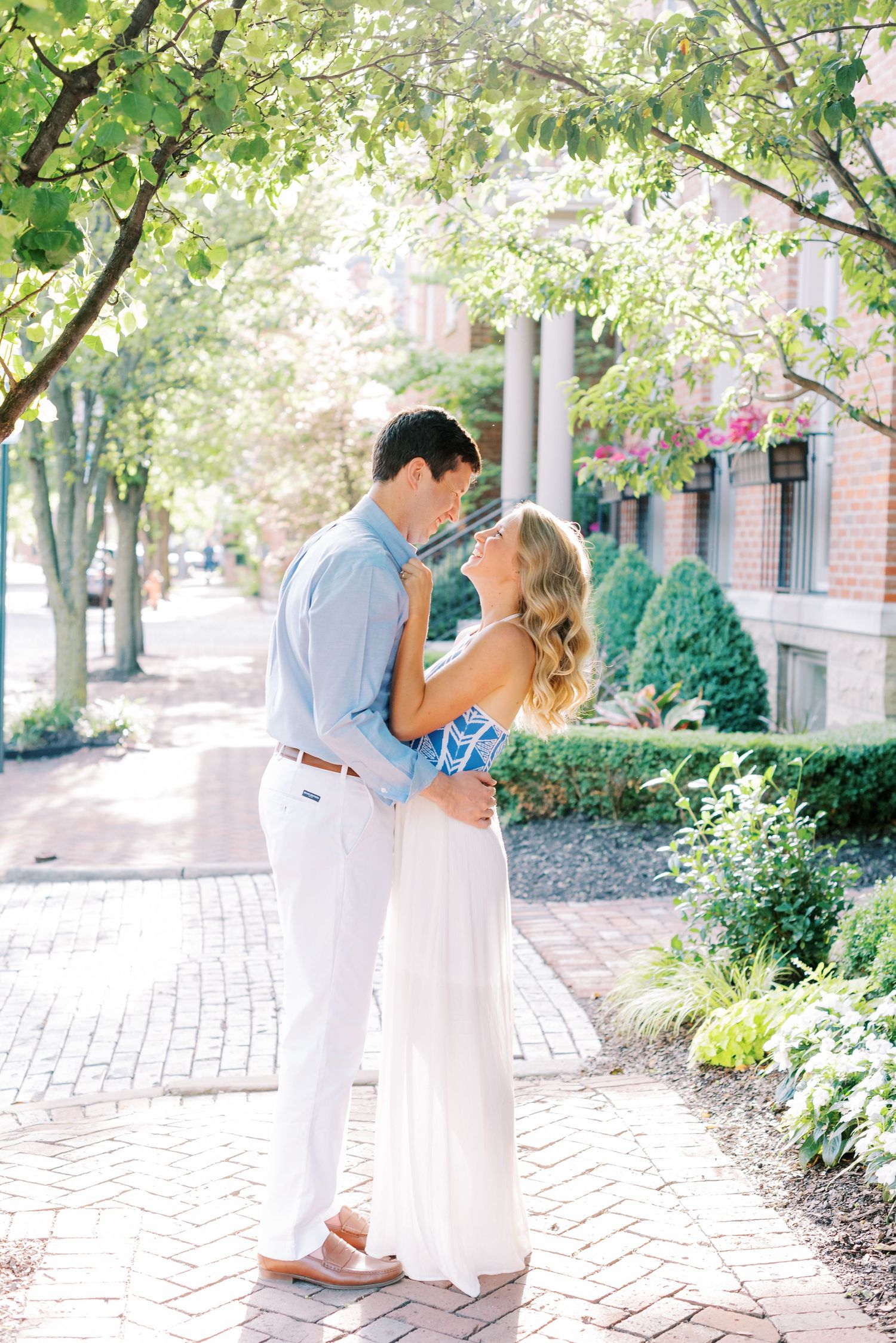 A romantic couple shares an intimate moment on a brick pathway surrounded by lush greenery and trees.