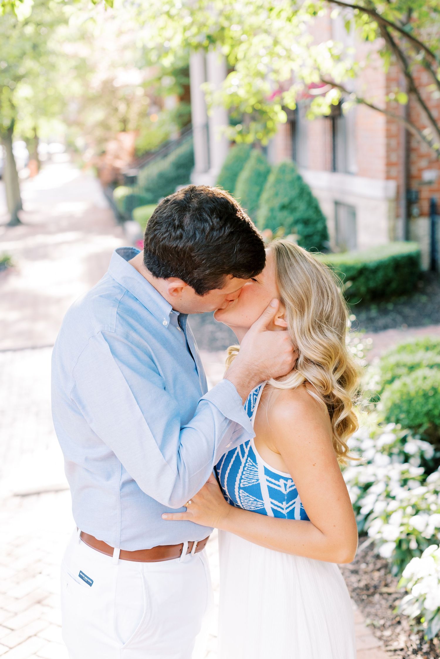 A romantic couple shares tender kisses while wearing coordinated blue and white outfits in a garden setting.