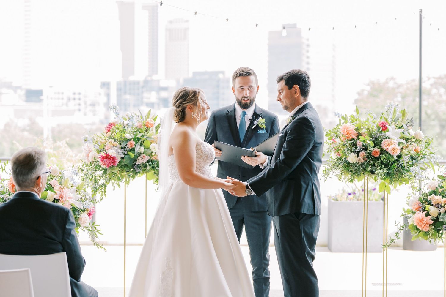 A joyful wedding ceremony takes place in a bright indoor venue with floral arrangements and natural lighting.
