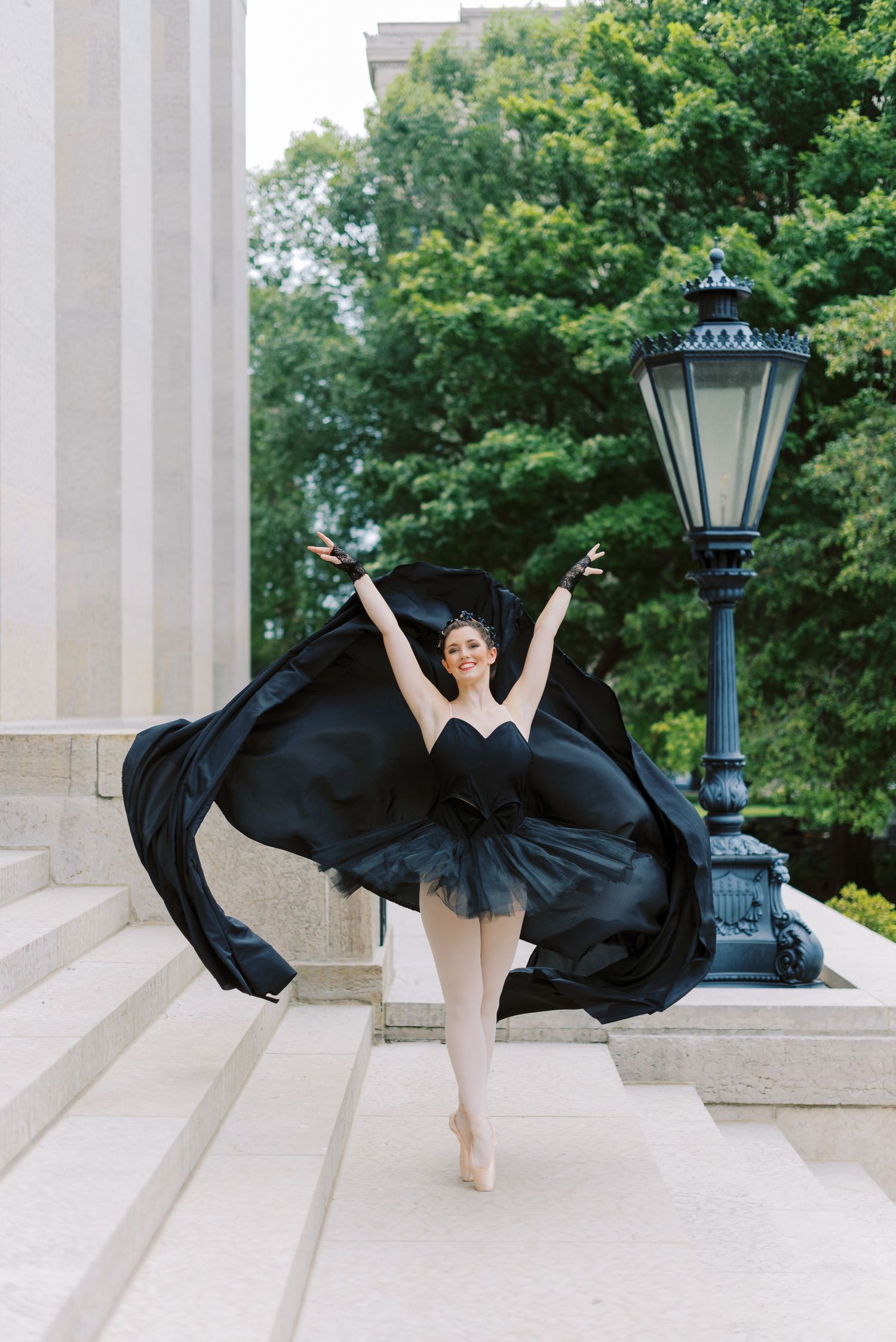 Dancer in flowing black dress performing elegant movements between classical columns.
