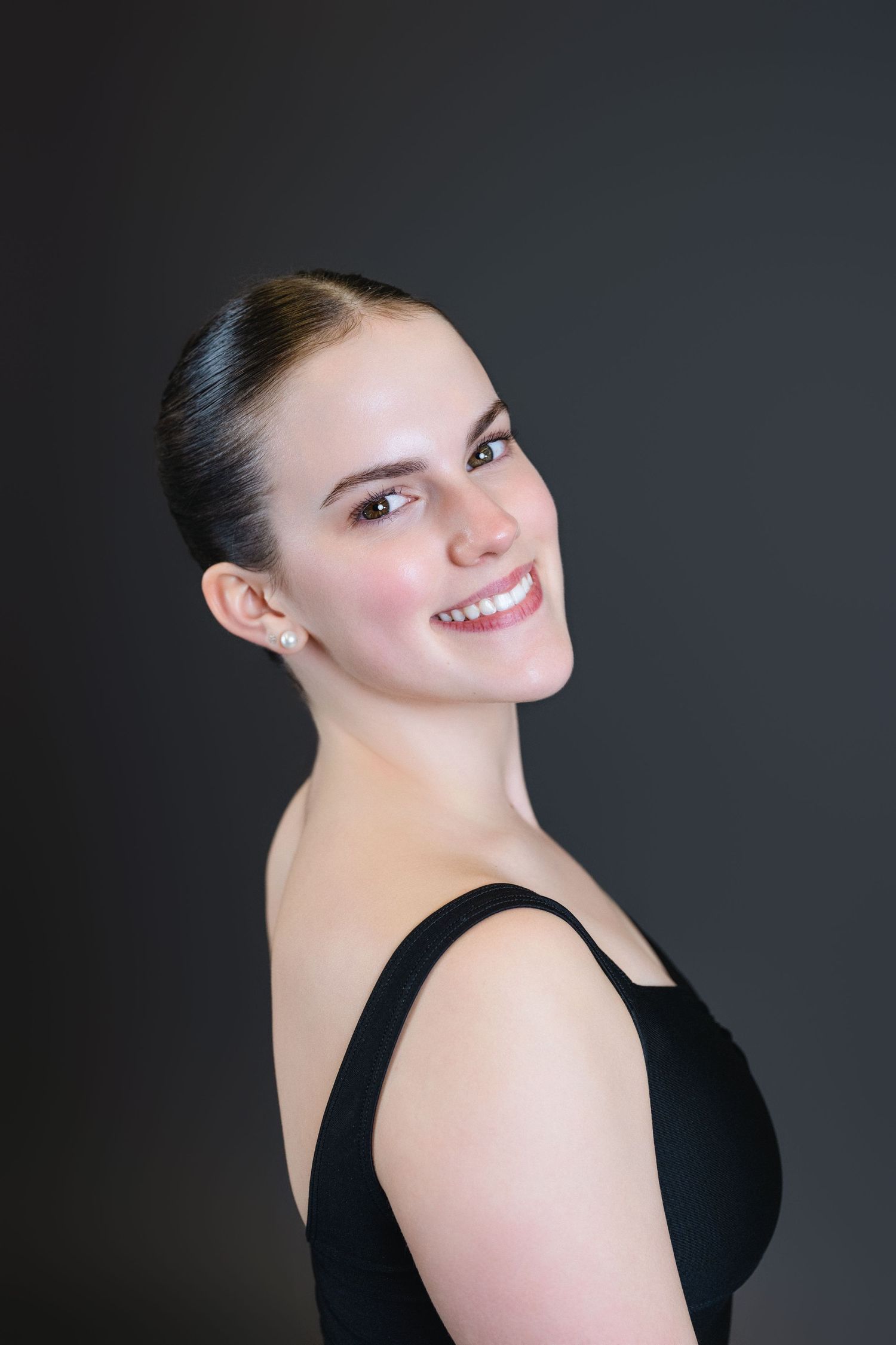 A figure in a black sleeveless top poses against a dark background with a bright smile and elegant posture.