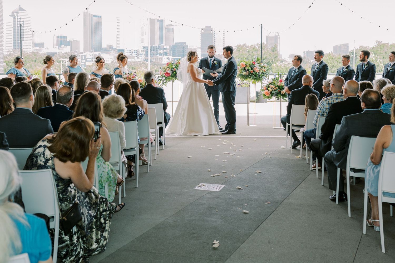 Wedding guests seated in rows during an outdoor ceremony with city skyline views in the background.