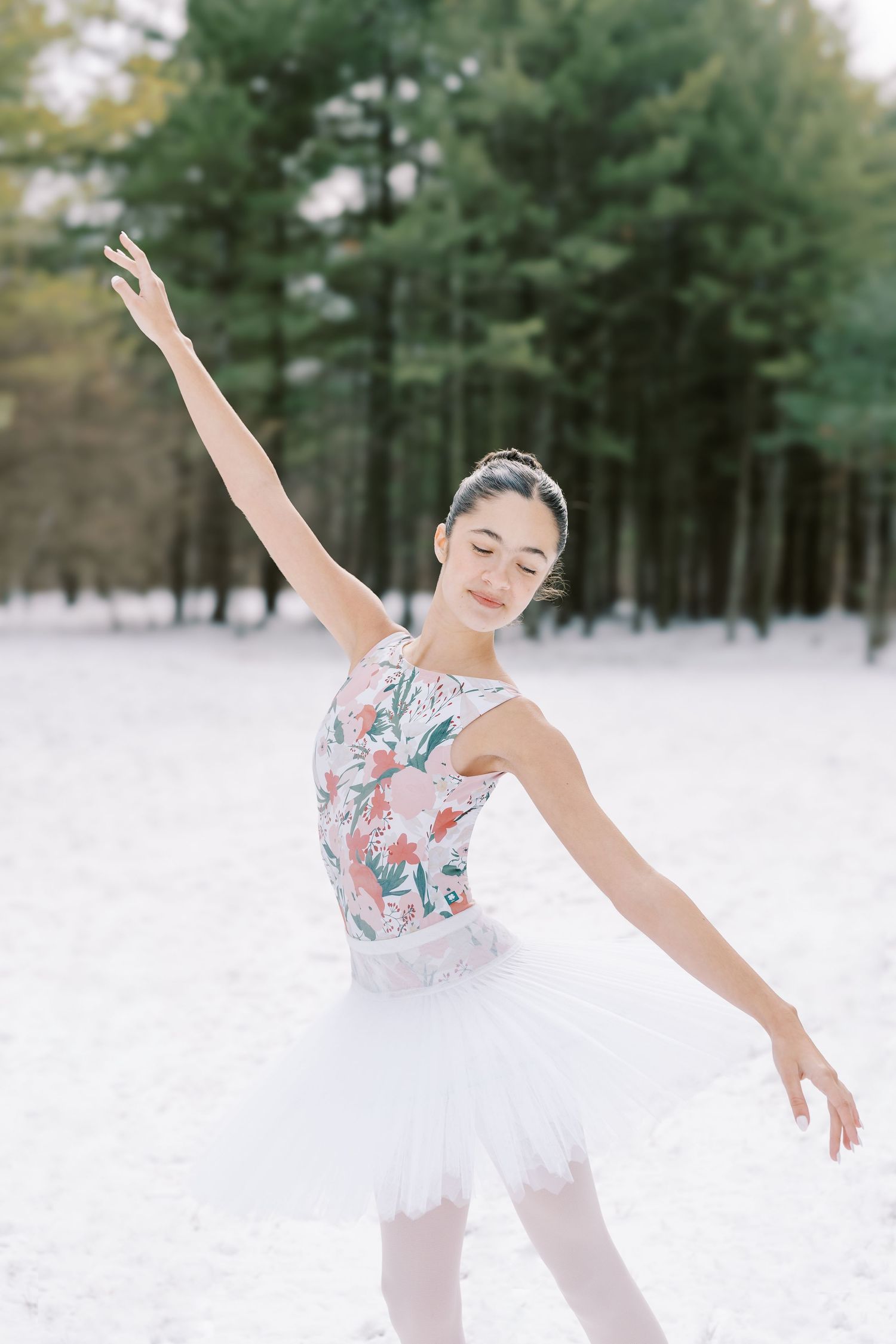 Ballet dancer in floral leotard performs graceful poses in snowy winter forest setting.