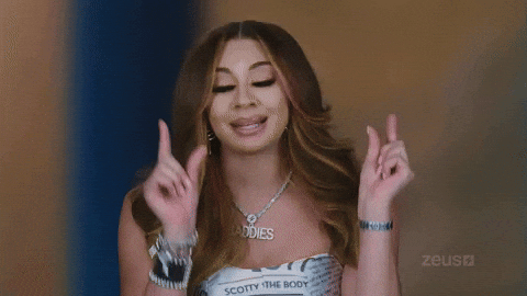 Young woman in stylish outfit making peace signs with both hands, wearing layered necklaces and bracelets.