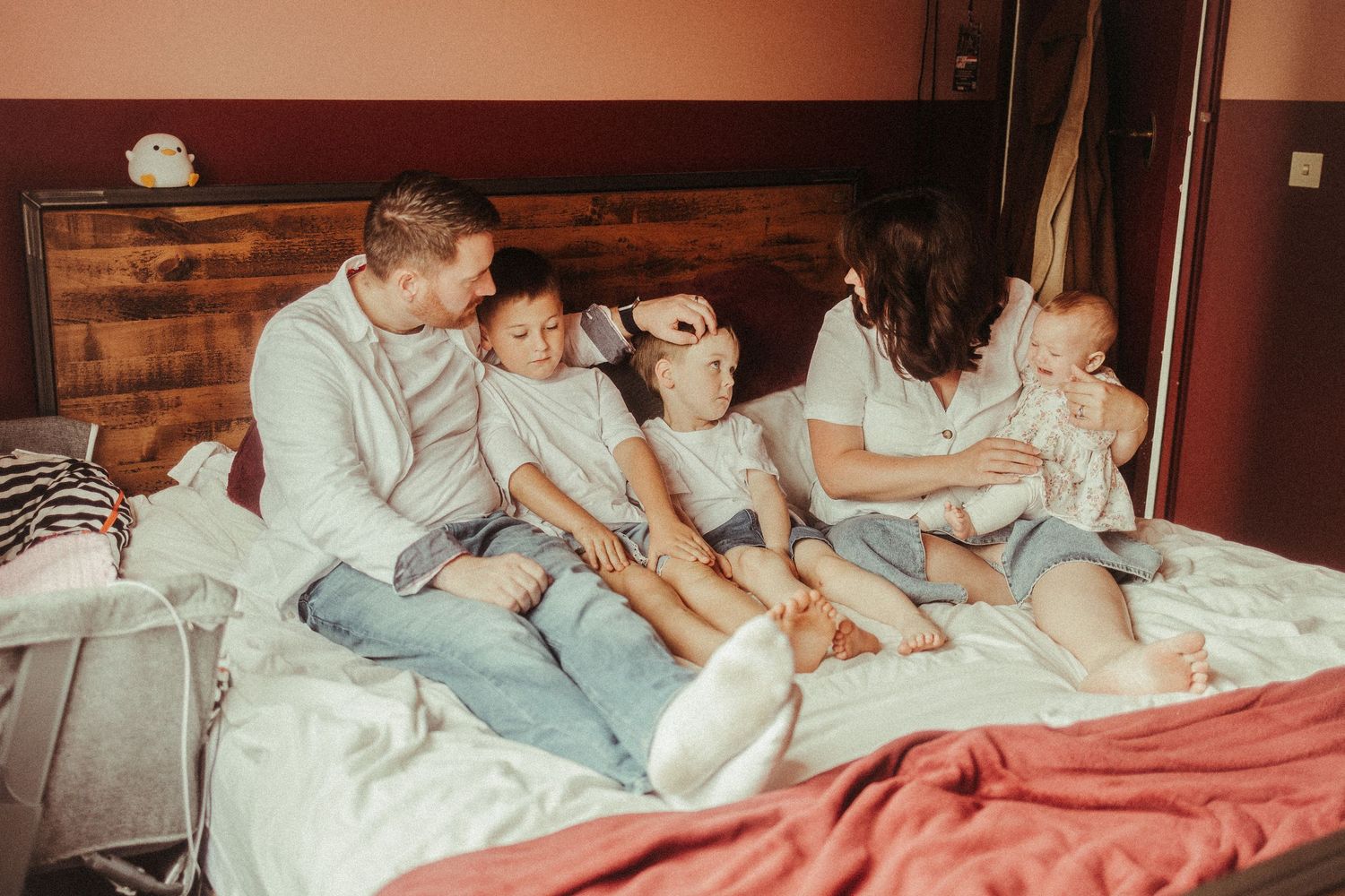 Family of five sitting together on a bed, parents and three young children in matching gray outfits, sharing a warm moment.