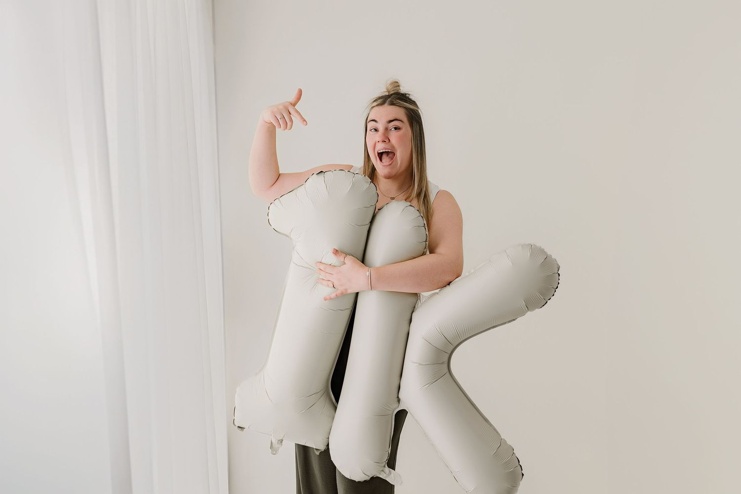 Woman excitedly holding large inflatable letter balloon against white background.