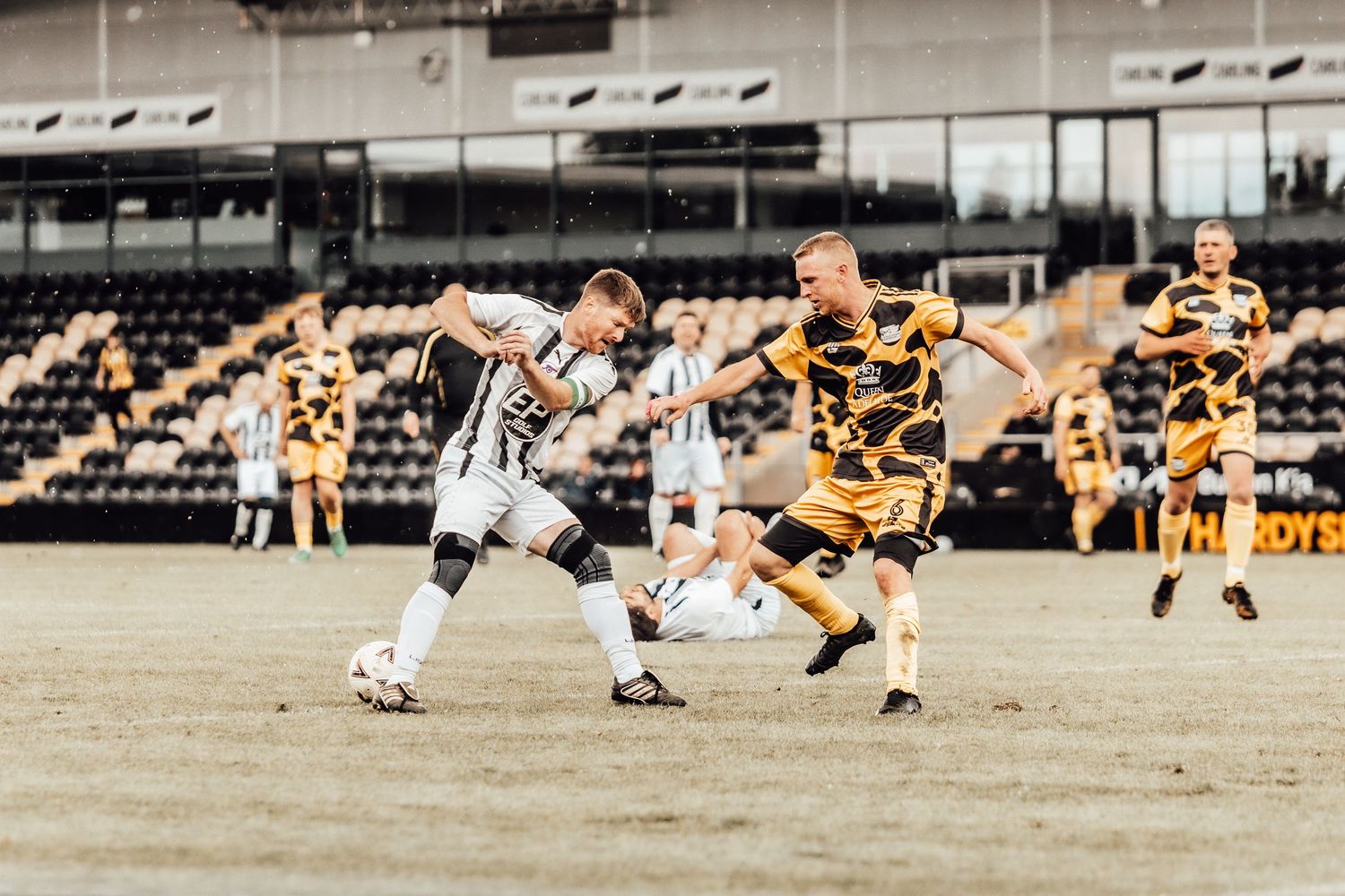 Two soccer players compete for the ball during a match at a stadium with yellow and black team colors.
