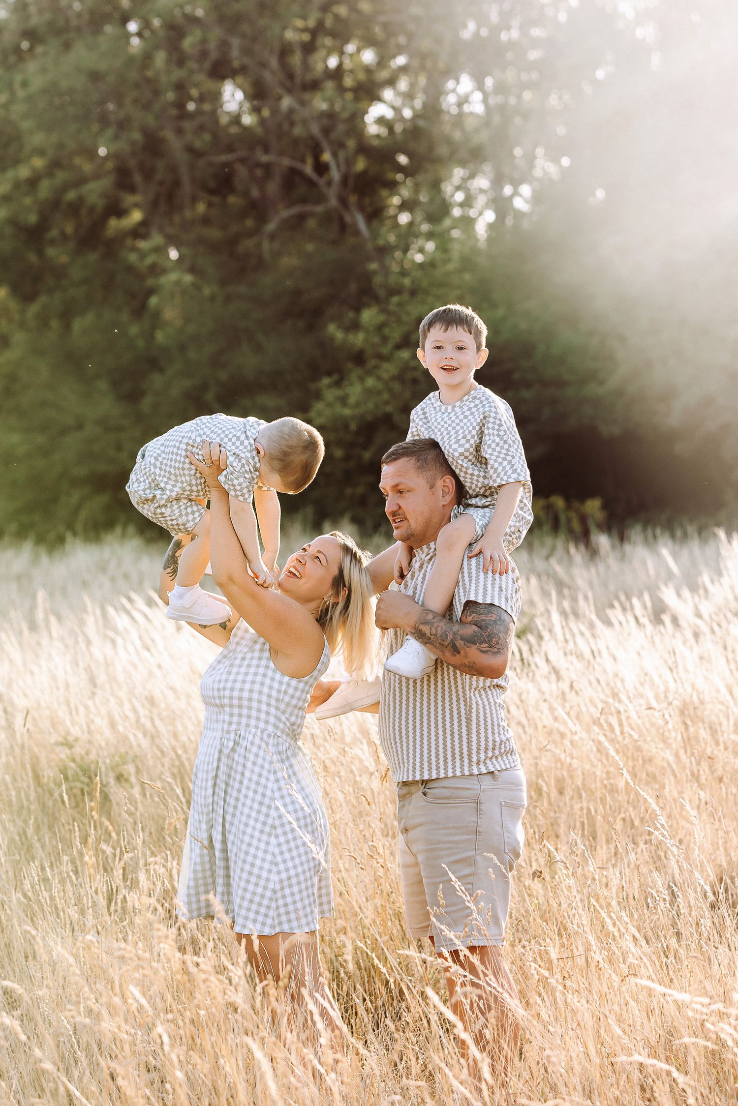 Happy family with two young children playing in a sunlit golden field, parents lifting kids with joy.