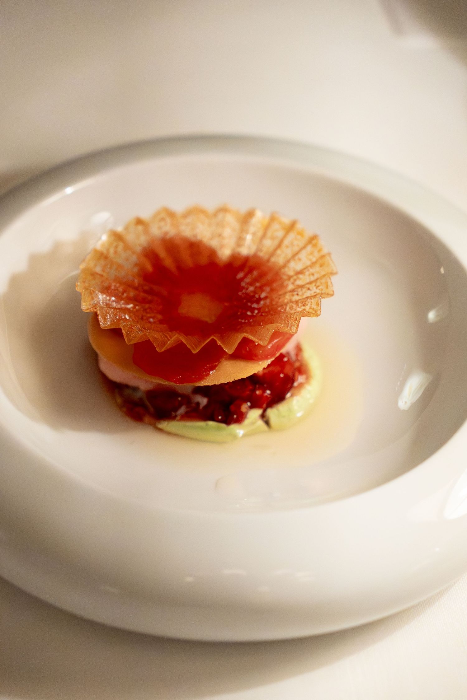 Elegant fine dining dish with layered tomato, cream, and berry compote topped with a delicate crispy wafer on a white plate.