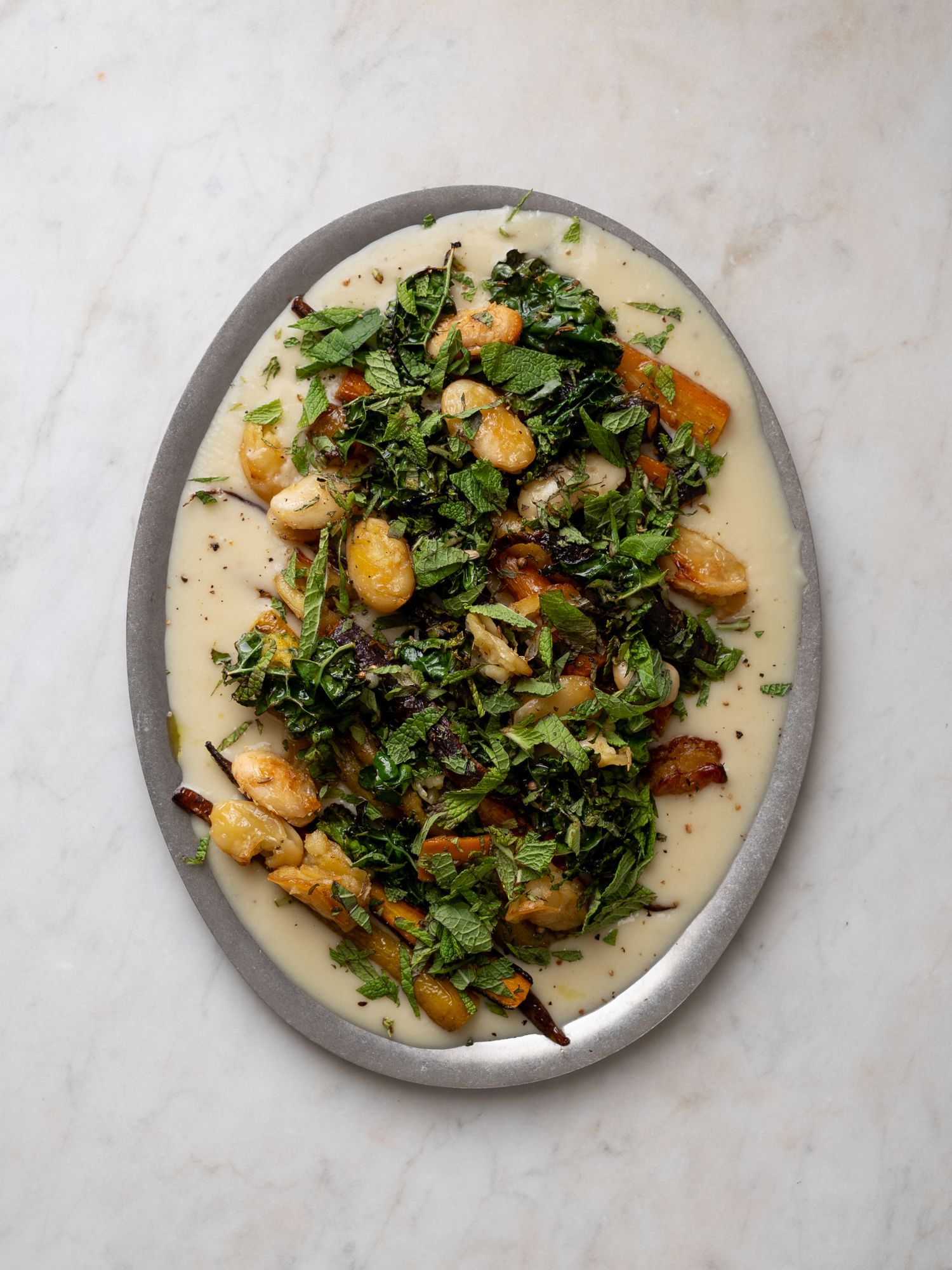 Oval platter of roasted gnocchi and crispy kale over creamy white sauce on marble surface.