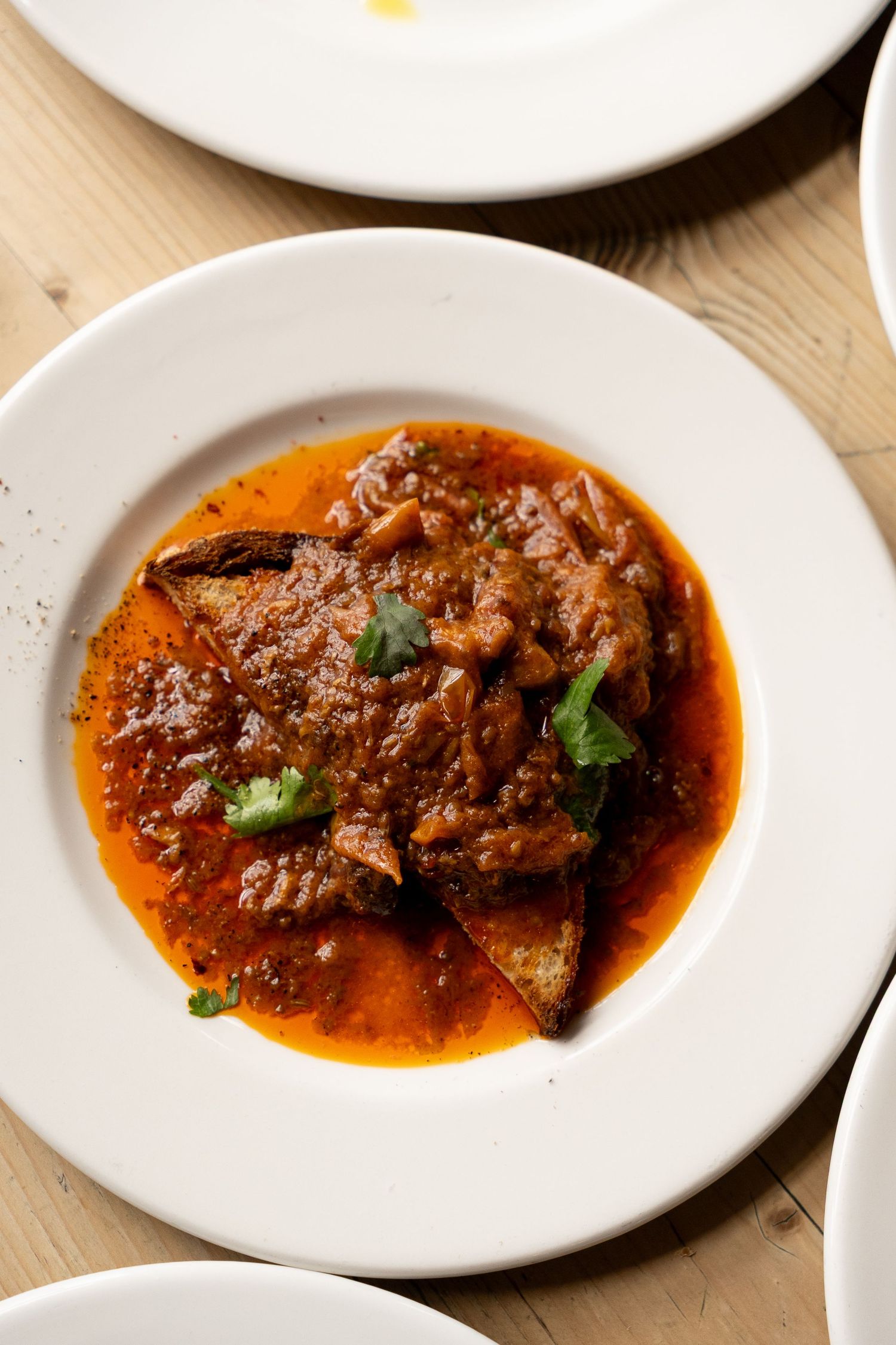 Rustic braised beef in rich tomato sauce garnished with fresh cilantro served in white ceramic bowl.