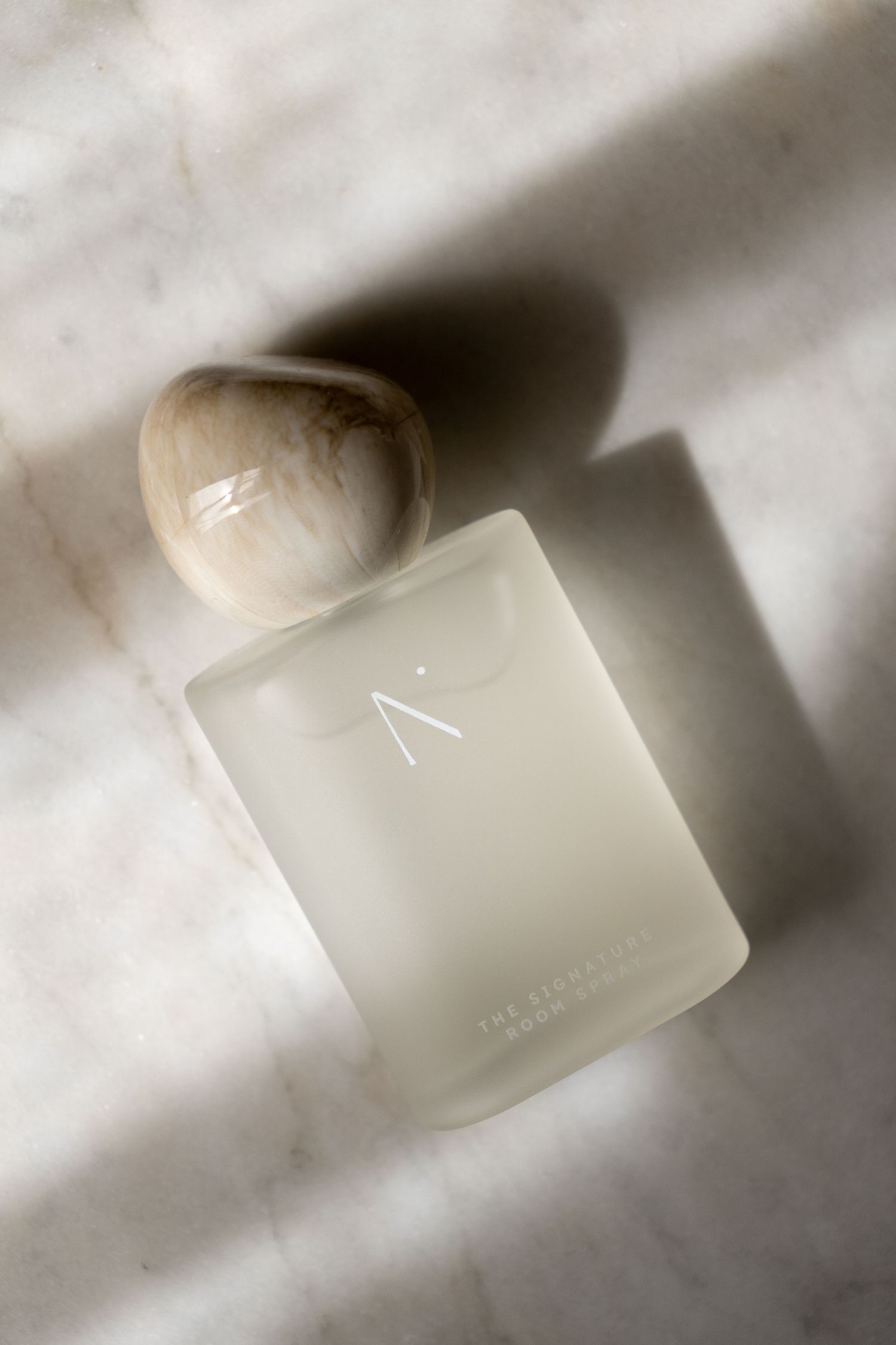 Frosted glass N. Signature Room Spray bottle with marble stone cap resting on white marble surface in natural light.