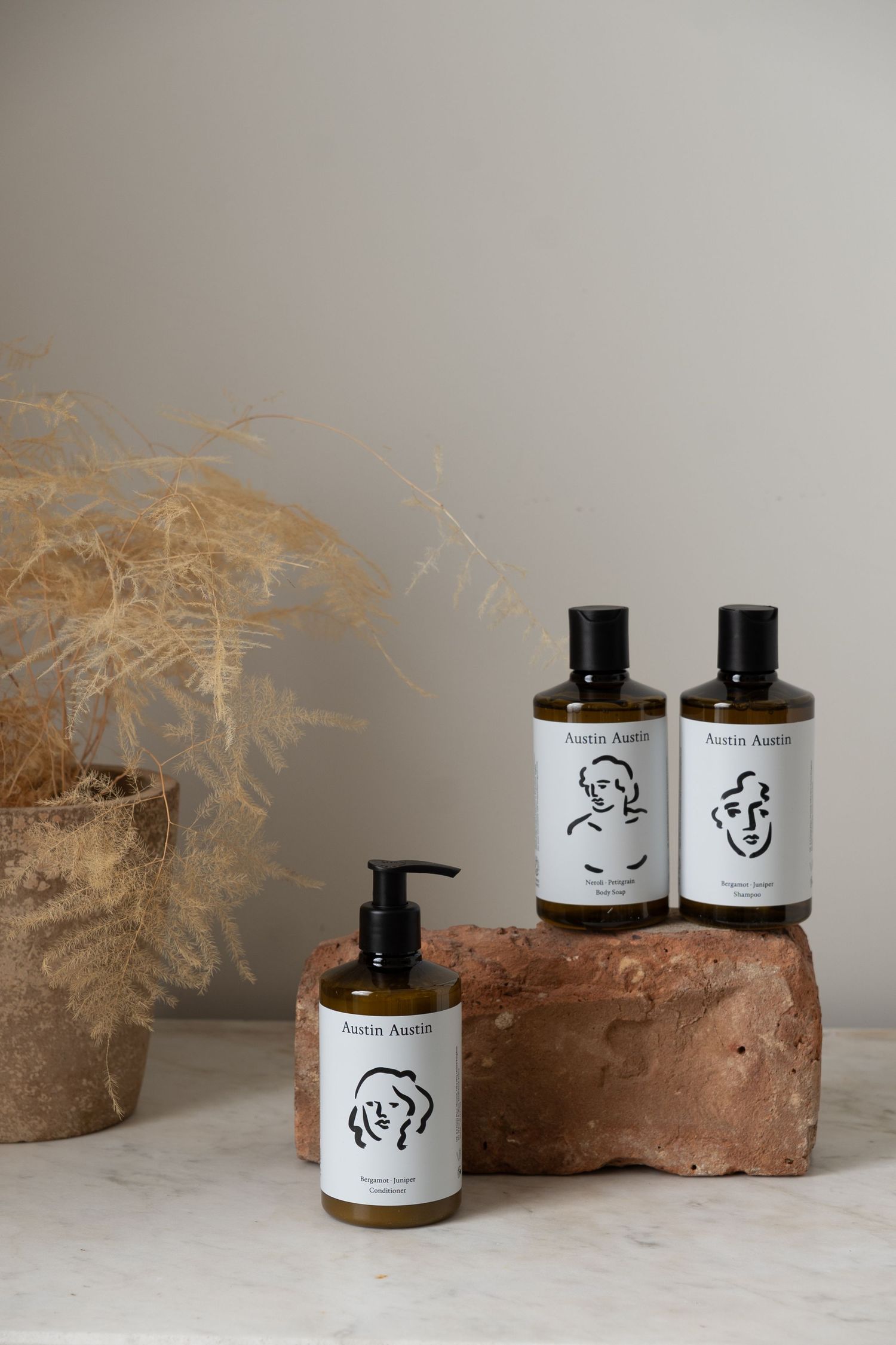 Austin Austin natural hair care products displayed on a rustic stone with dried botanicals in a terracotta pot.