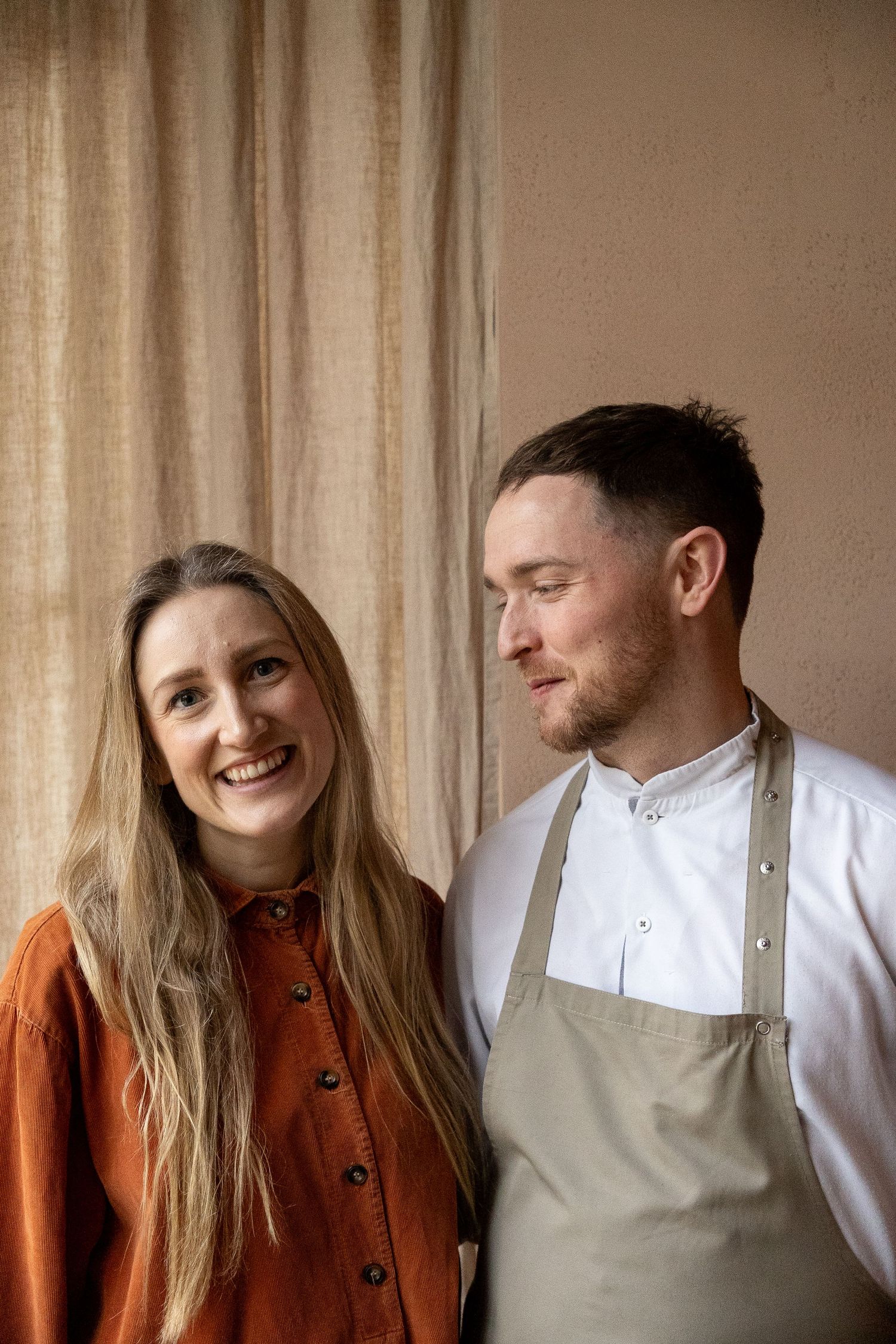 Smiling female front-of-house and male chef in apron posing together at restaurant.
