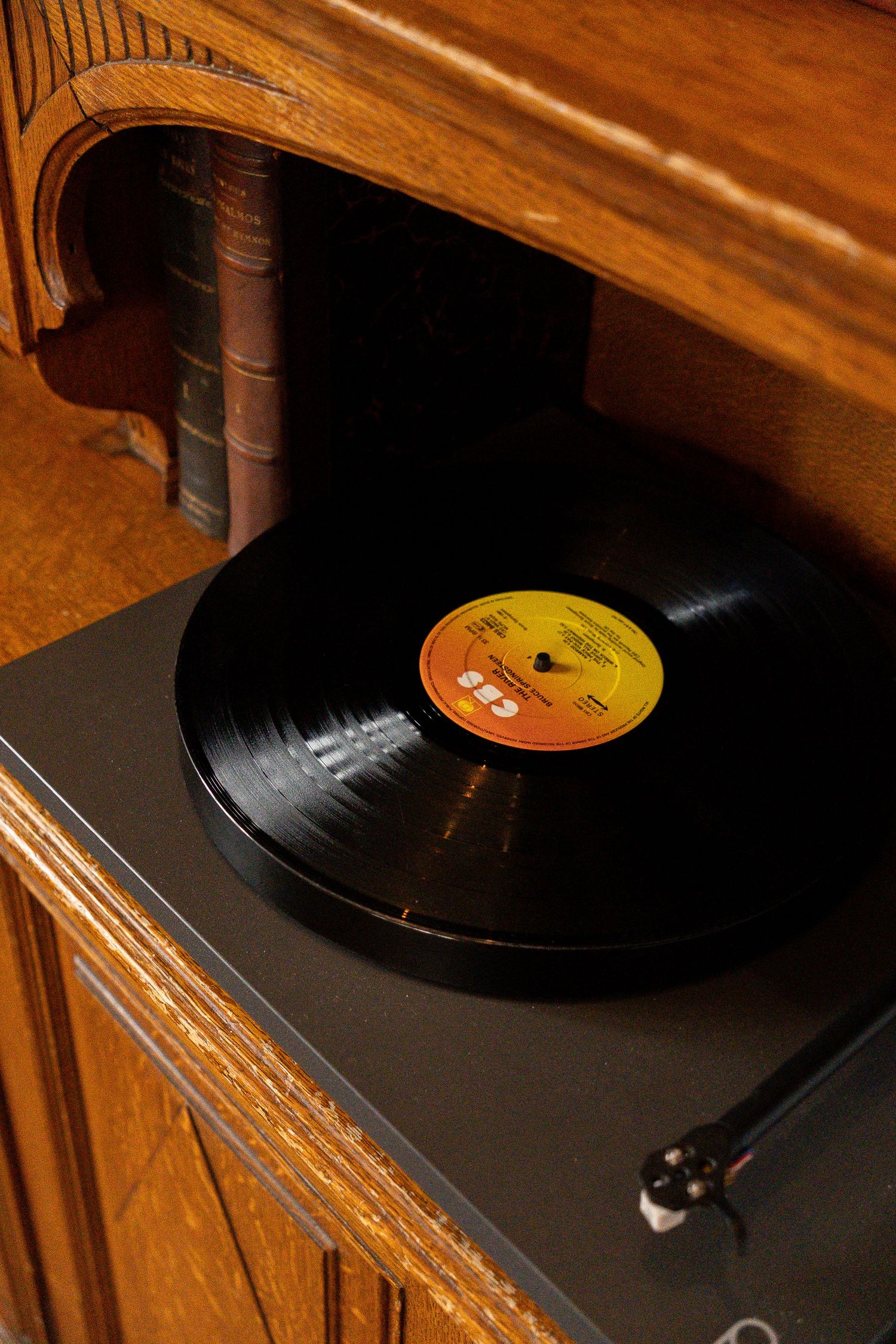 Vintage black vinyl record playing on turntable built into antique wooden cabinet with warm golden lighting.