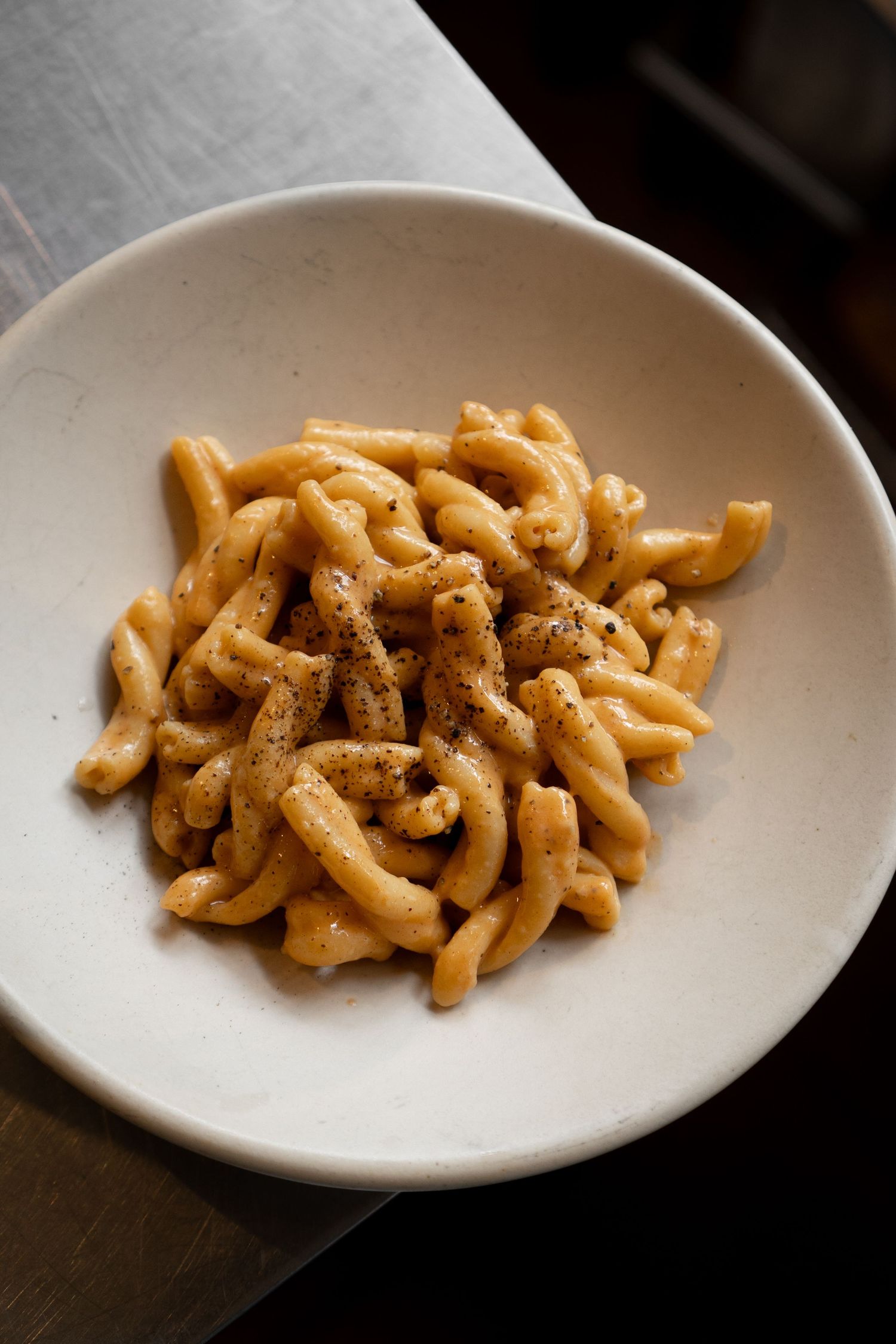 A white ceramic bowl filled with handmade cavatelli pasta tossed in a creamy tomato sauce with black pepper.