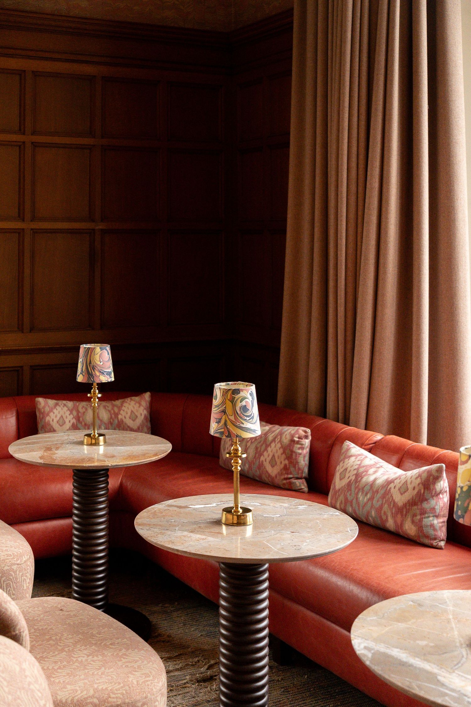 Elegant restaurant lounge with curved red leather sofas, marble side tables, and decorative brass table lamps.