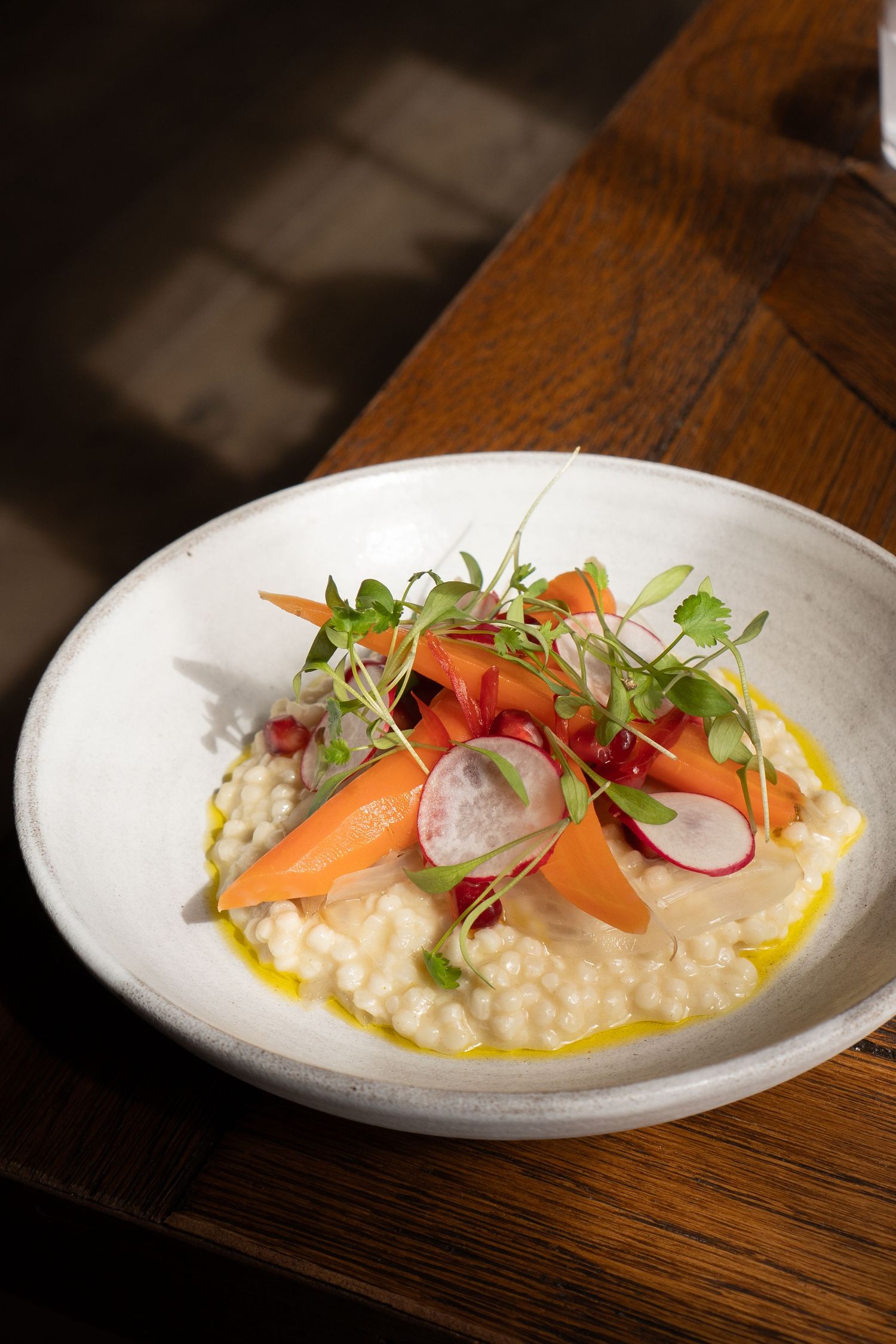 Risotto dish topped with glazed carrots, radish slices, and fresh microgreens on white plate.