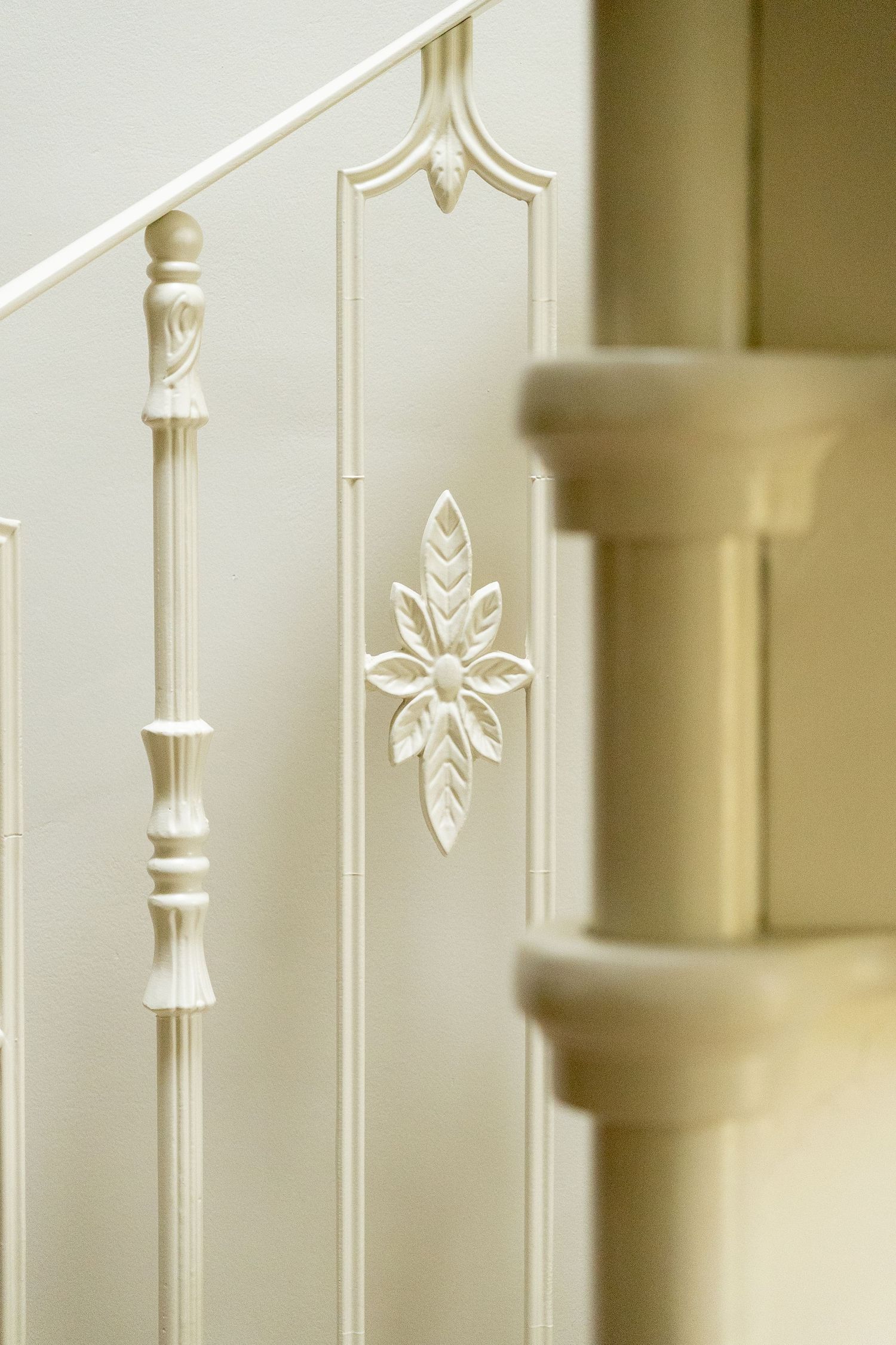 Detailed close-up of cream-painted decorative staircase balustrade with carved floral motif and turned spindles.