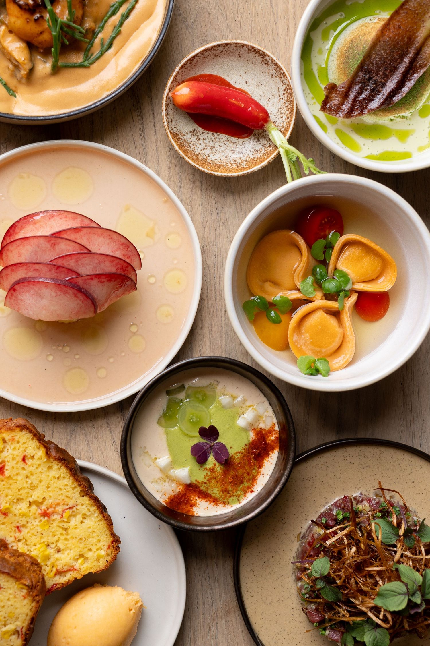 An elegant spread of gourmet dishes including pasta, bread, soups, and garnished plates arranged on a wooden table.