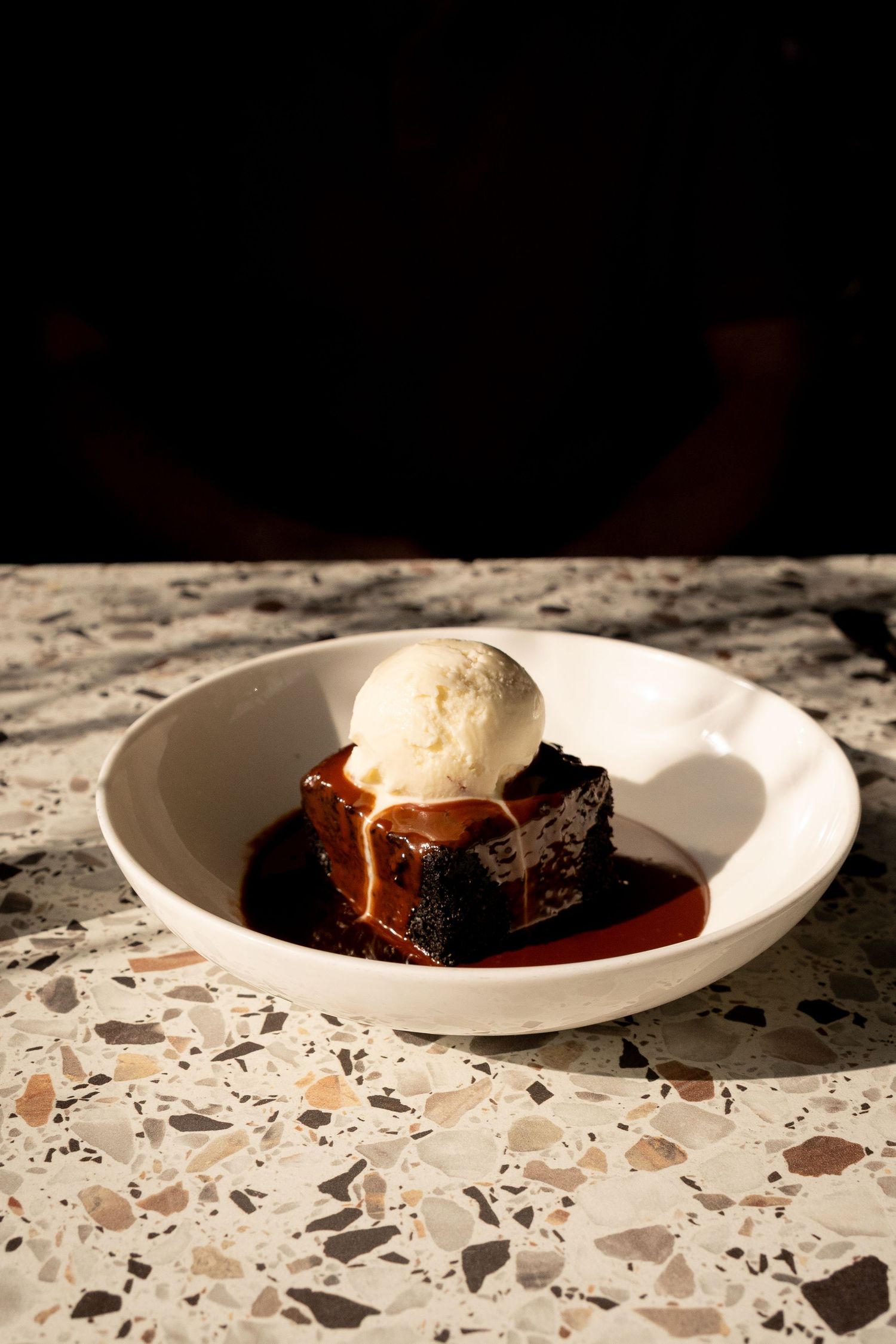 Decadent sticky date pudding with caramel sauce topped with vanilla ice cream scoop served in white bowl.