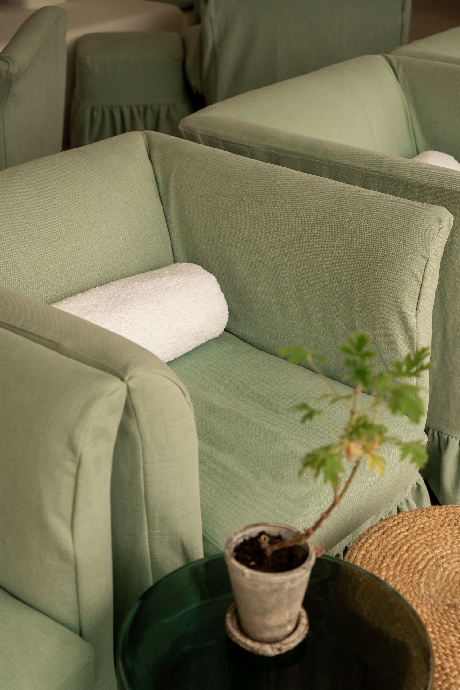Close-up of a sage green armchair with a rolled white towel and small potted plant on a dark side table.