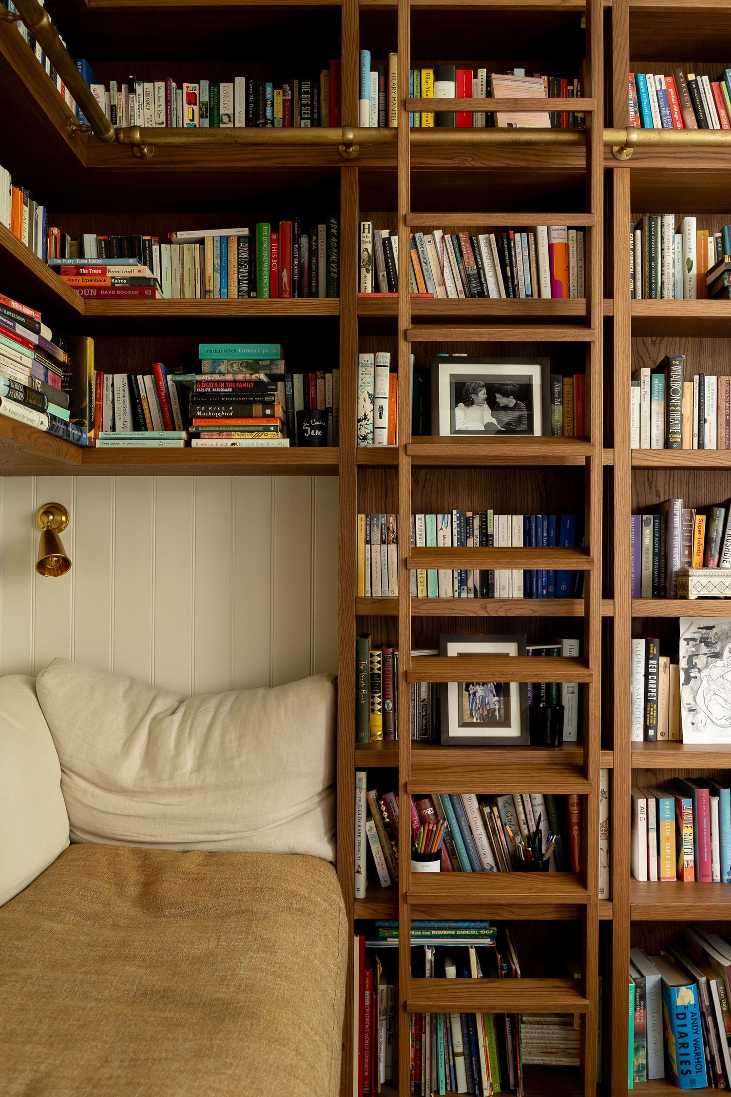 Floor-to-ceiling wooden bookshelves filled with books surrounding a cozy cream sofa reading nook.