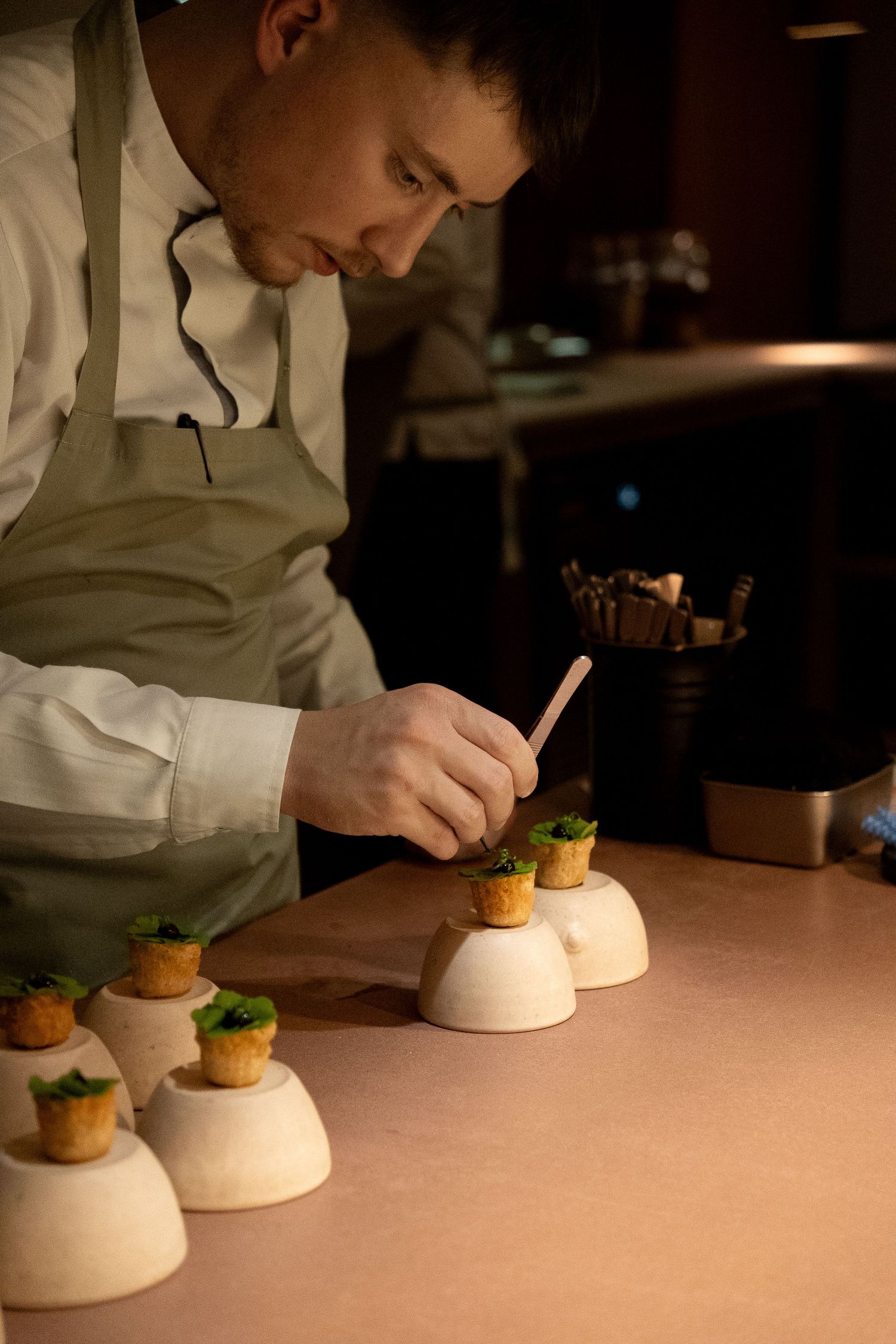 Chef carefully garnishing elegant canape appetizers displayed on white dome pedestals in a fine dining kitchen.