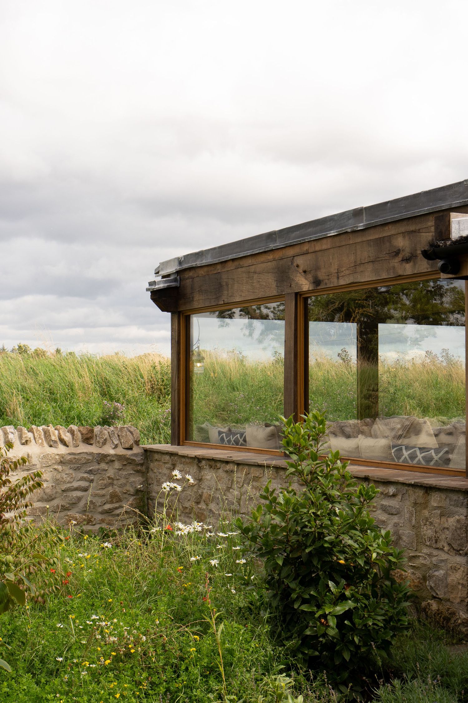 Rustic stone and wood glass-walled structure surrounded by wild meadow grasses.