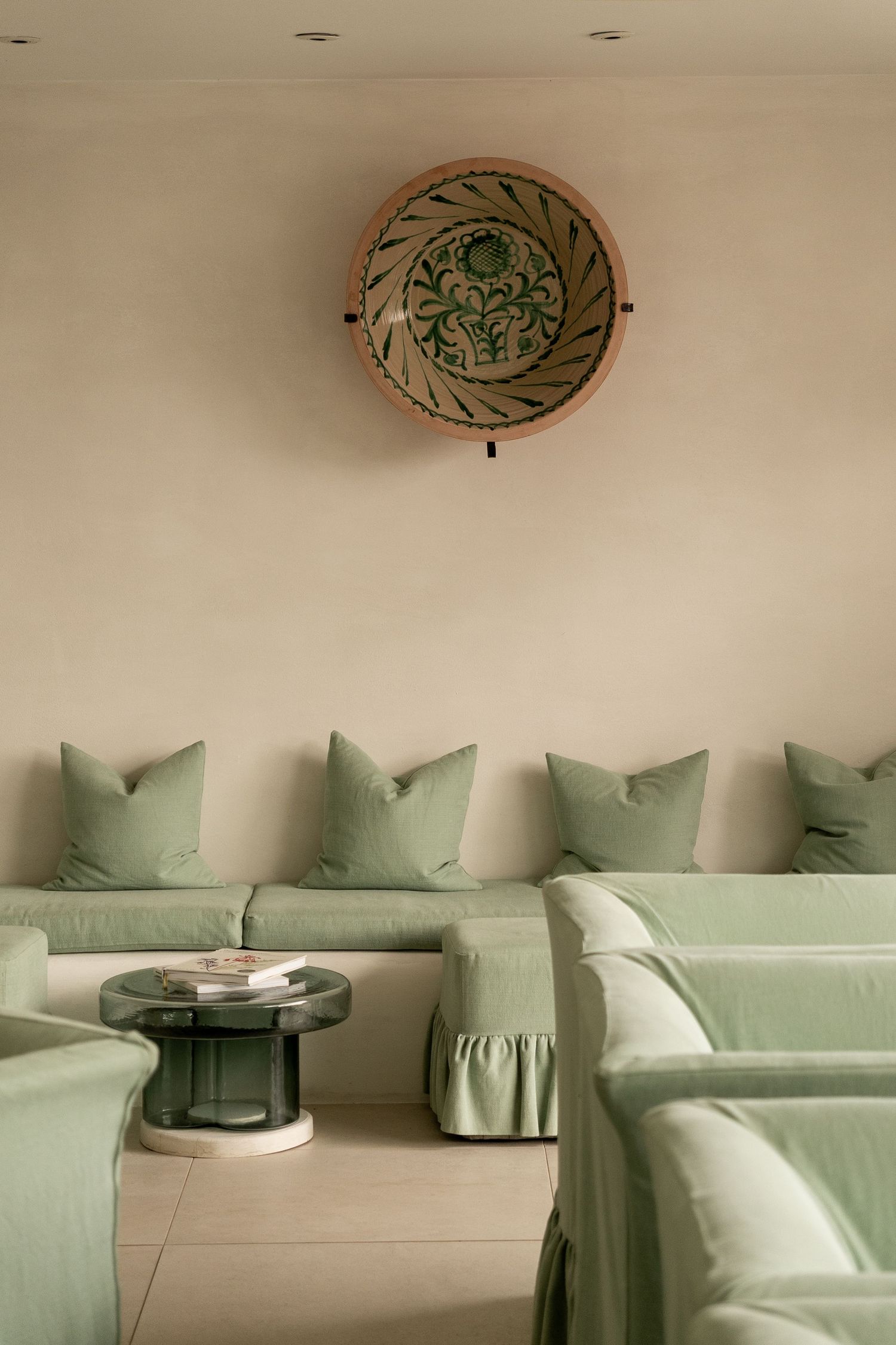 Elegant lounge with sage green slipcovered sofas, decorative wall plate, and round marble side table on neutral floor.