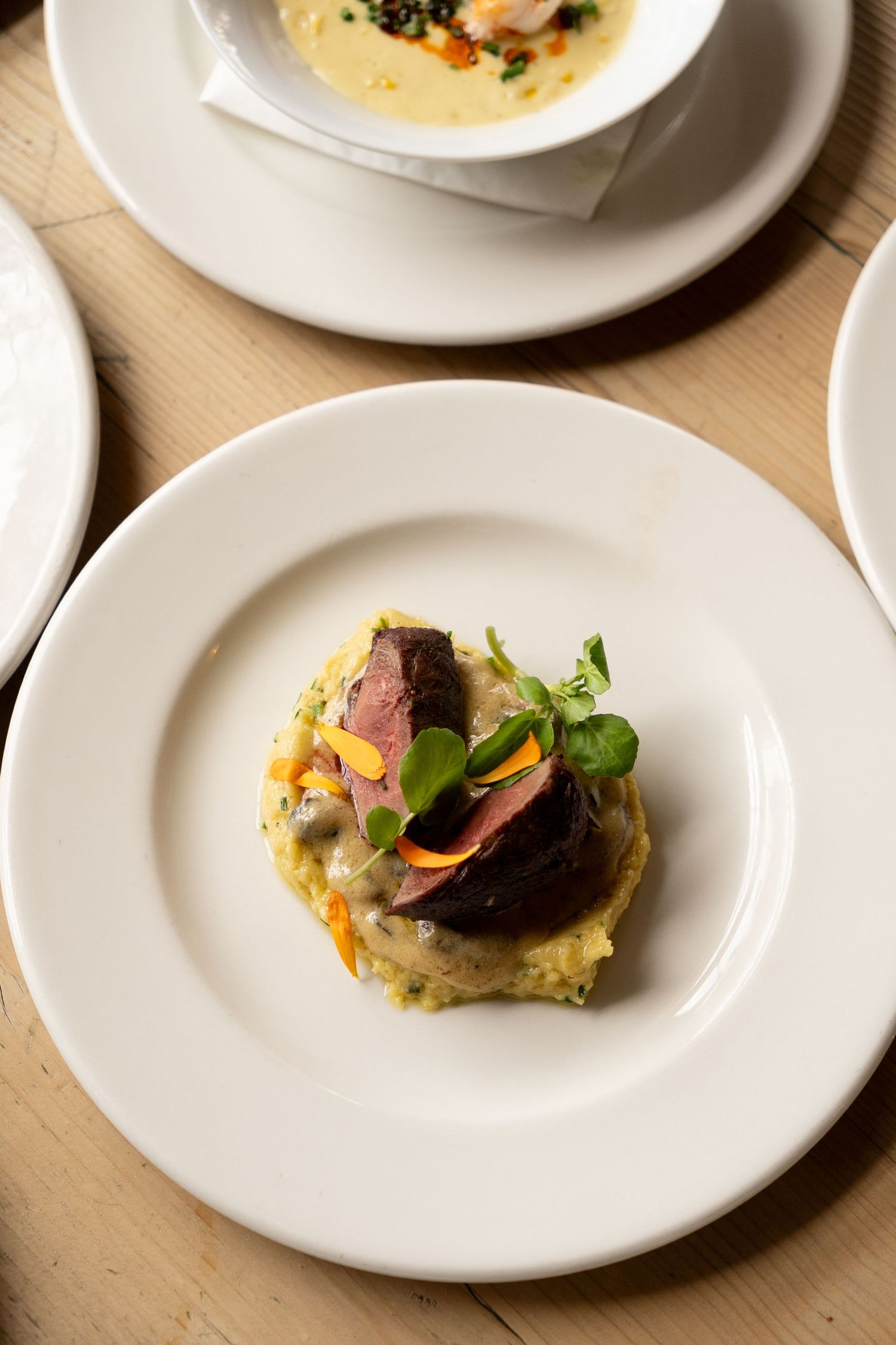 Elegant plated dish featuring sliced medium-rare meat atop creamy risotto, garnished with microgreens and carrot on white plate.