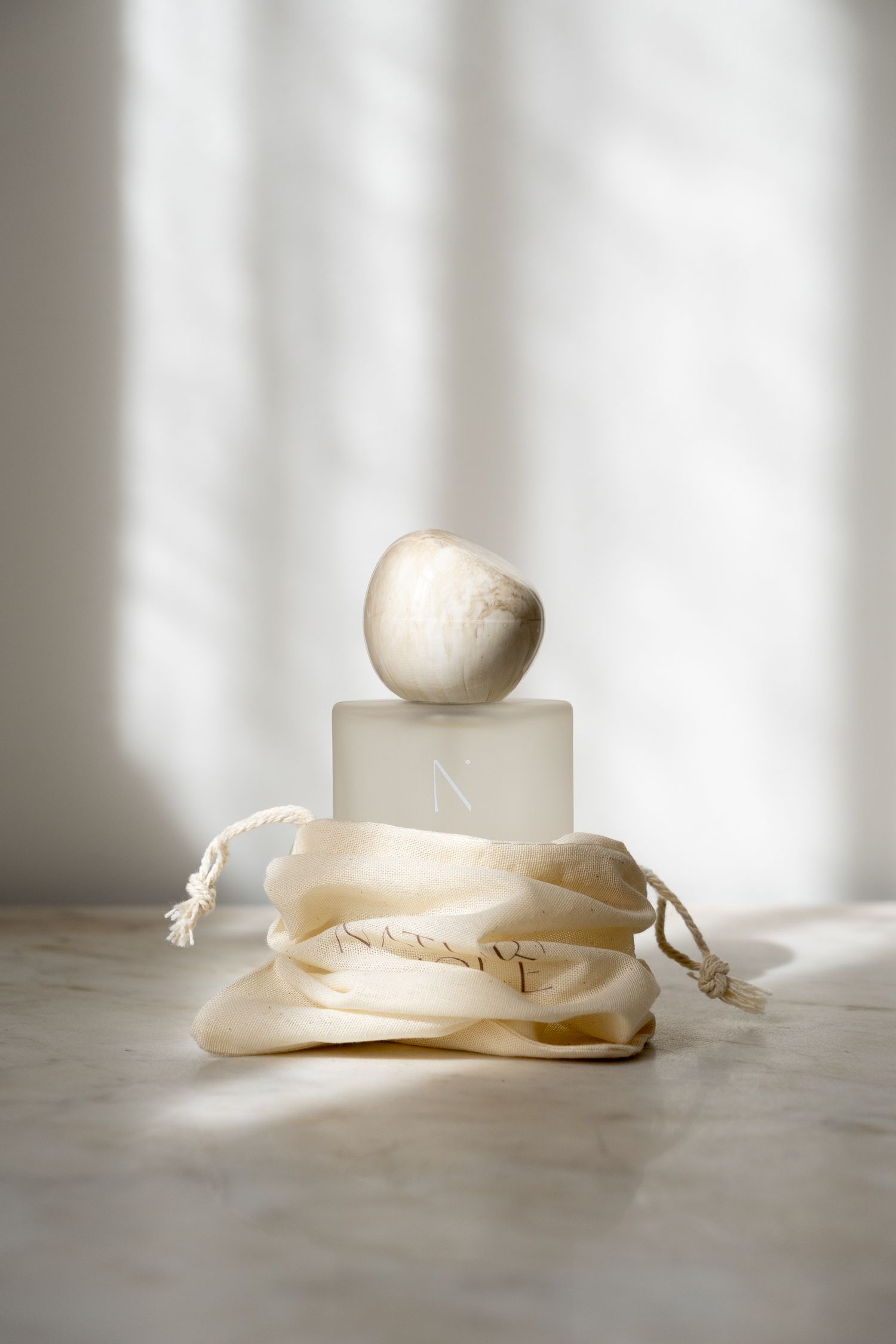 N. Signature Room Spray frosted glass bottle with marble stone cap displayed on cream linen pouch in soft light.